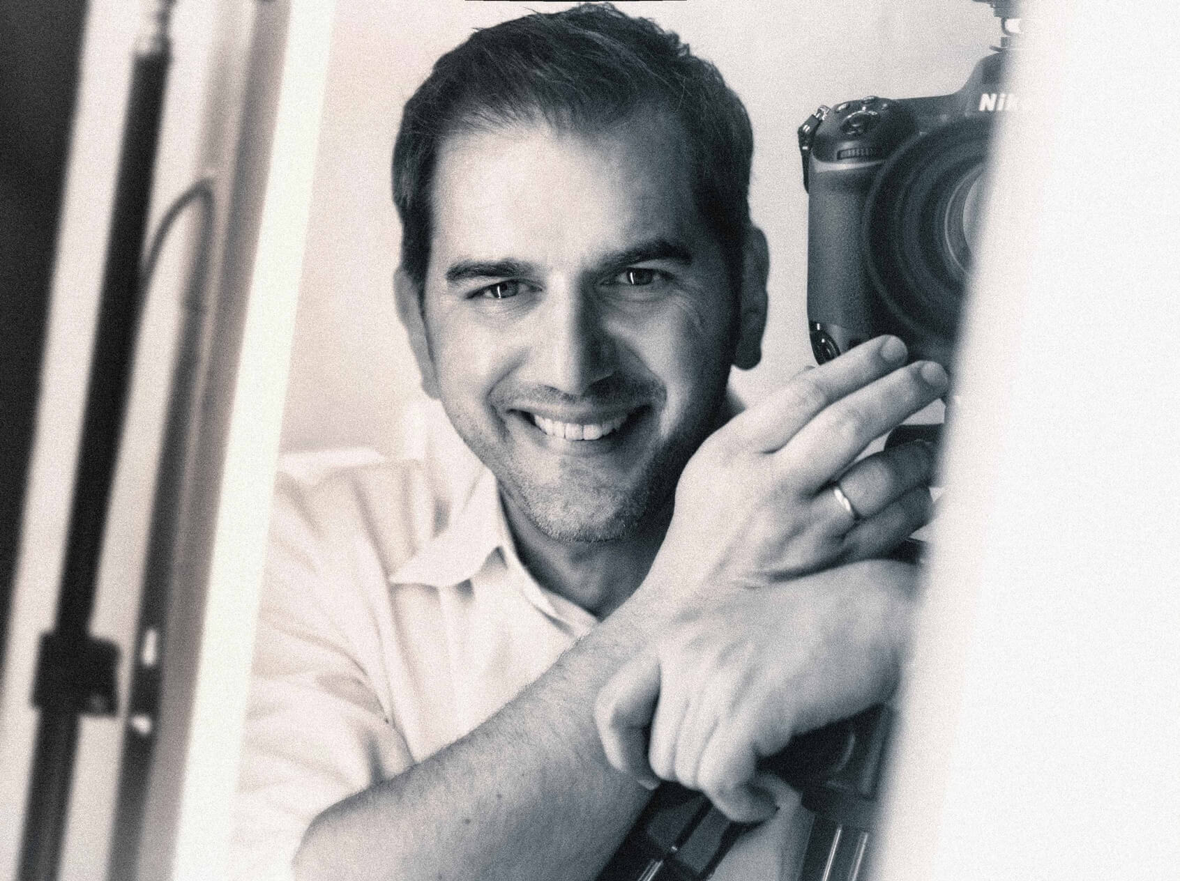 Der Fotograf Andi Bruckner hält eine Kamera in der Hand und lächelt.