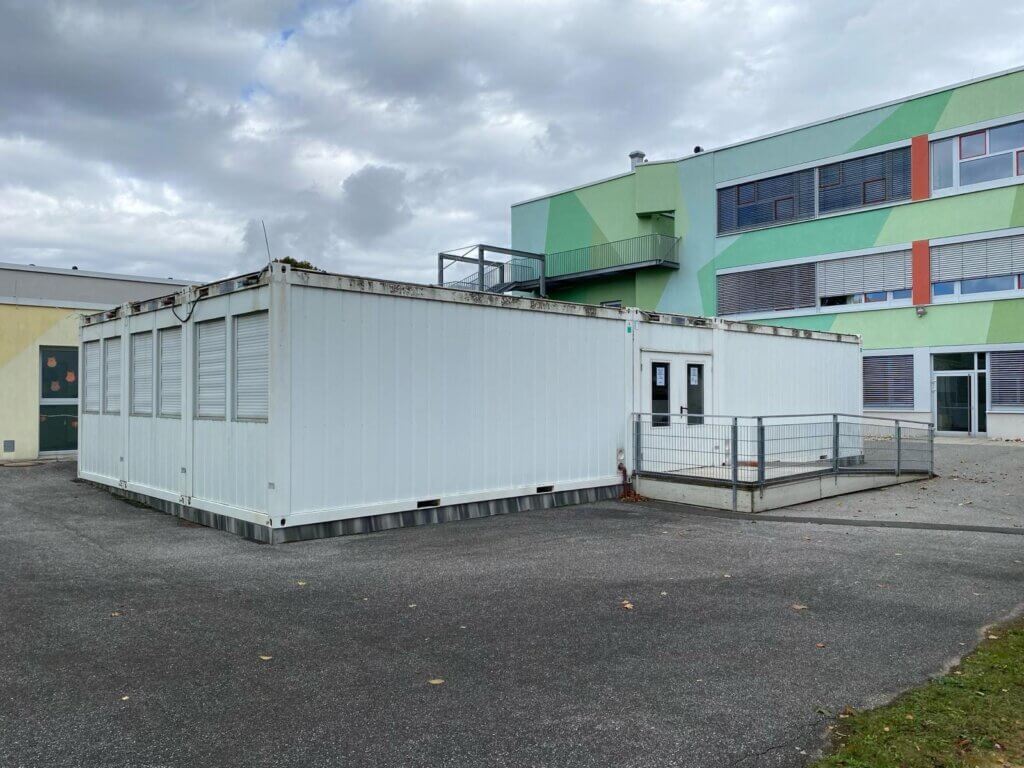 Die EMS Oberwart mit grüner Fassade. Davor sind Container zu sehen.