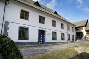 Das Haus von Trude Meichenitsch in ganzer Länge. Es ist ein Gebäude mit vielen großen Fenstern und einer blau-weißen Tür