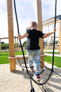 Kind in schwarzem T-Shirt spielt im Funkpark.Man sieht wie es auf einem Seil balanciert. Man sieht es von hinten