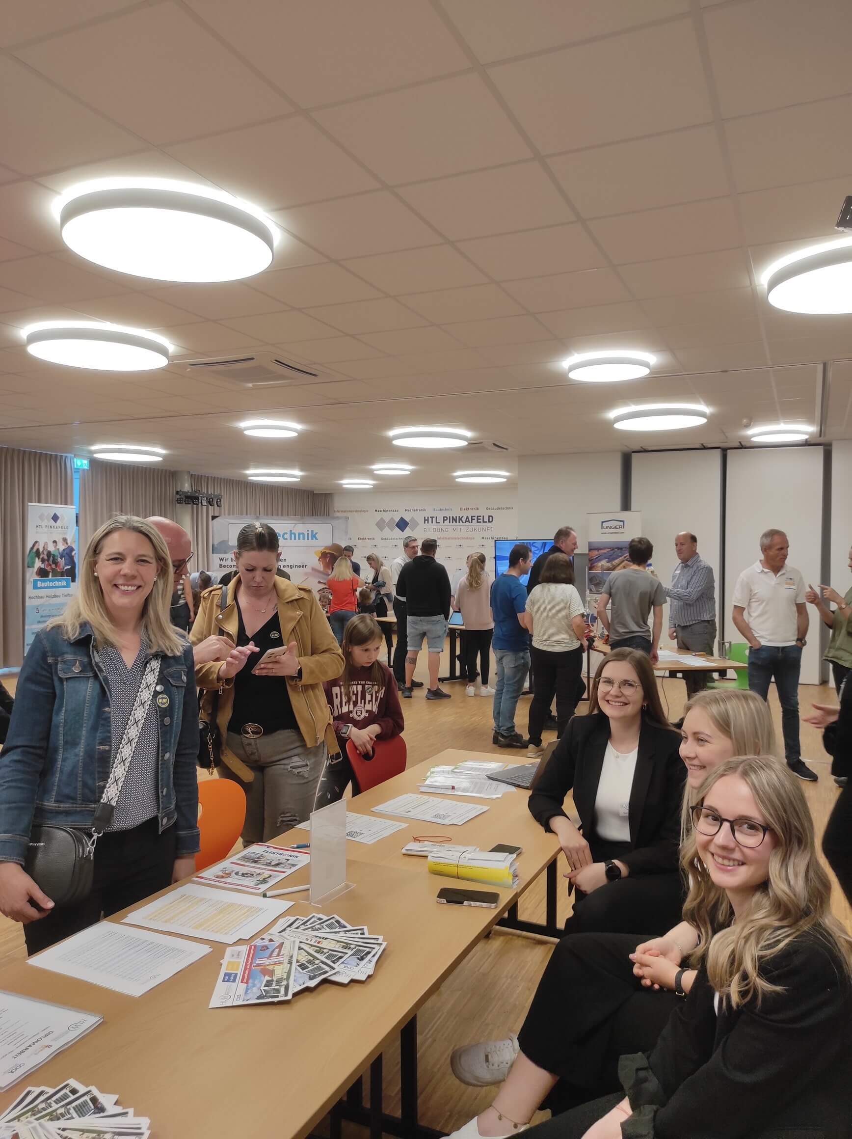 Besucherinnen informieren sich bei den Schülerinnen über die Typisierungsaktion. sie blicken in die Kamera und lächeln