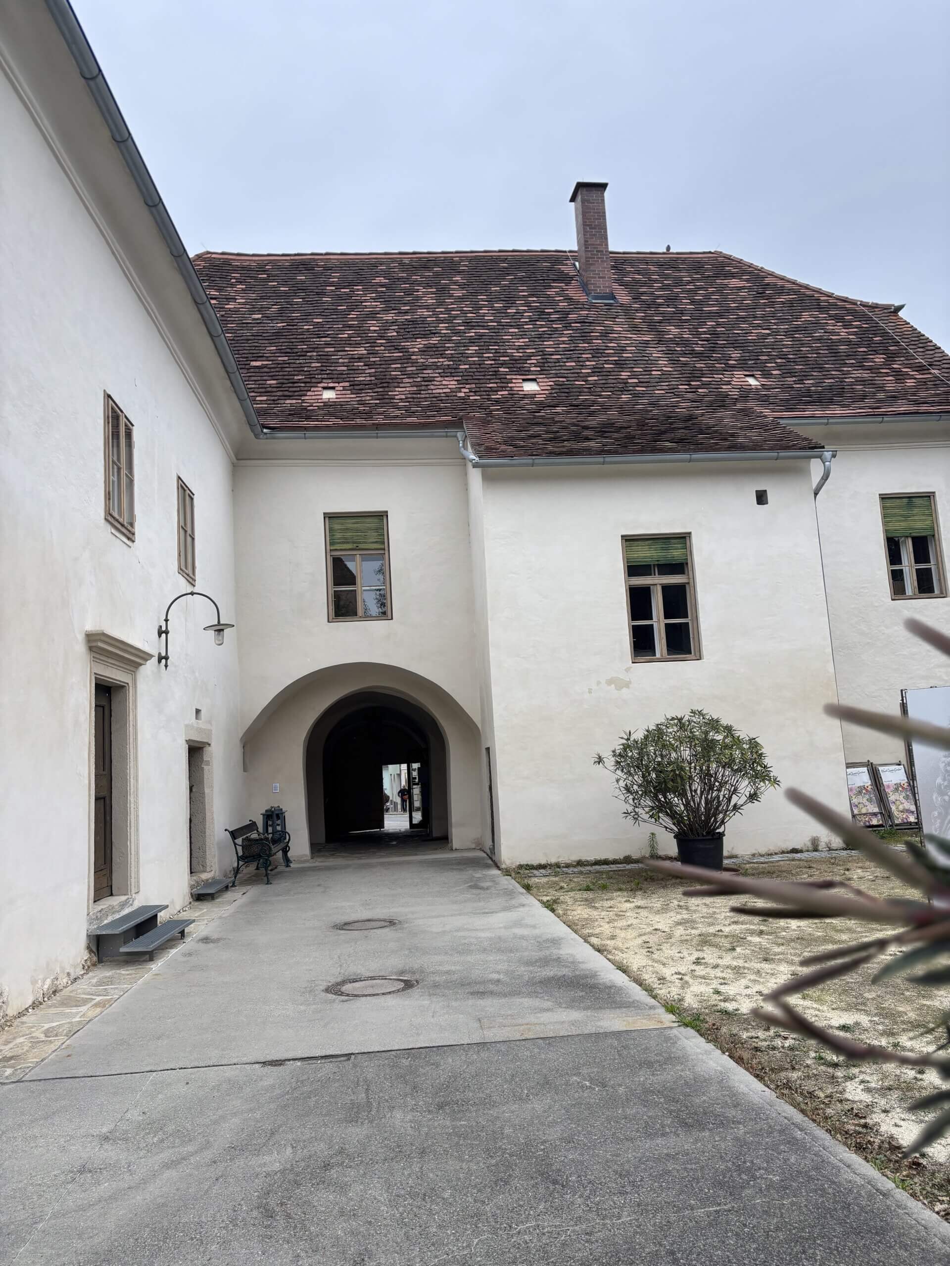 Ein weiterer Blick auf den Innenhof des Steinpeißhauses mit einem gewölbten Durchgang auf der linken Seite. Ein Topf mit einer Pflanze steht in der Mitte des Hofs.