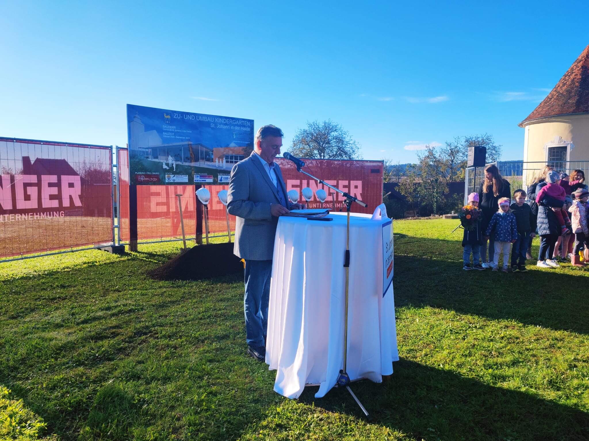 Ein Mann in einem hellgrauen Anzug steht hinter einem weißen Rednerpult.