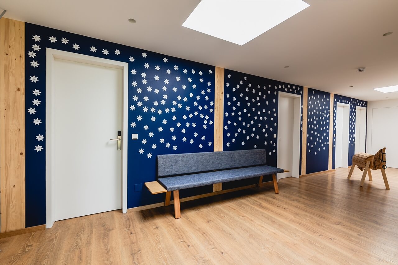 Moderner Warteraum mit blauen Wänden und weißen Sternen, Holzboden und blauer Bank für gemütliche Atmosphäre.