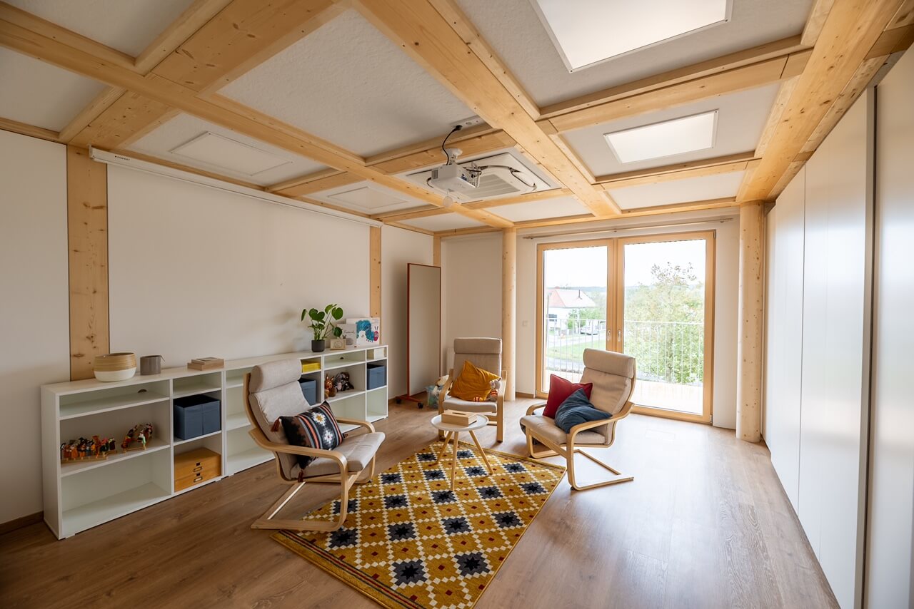Moderner Besprechungsraum mit gemütlichen Stühlen und Teppich unter Holzdecken, helle Fenster für natürliche Beleuchtung.
