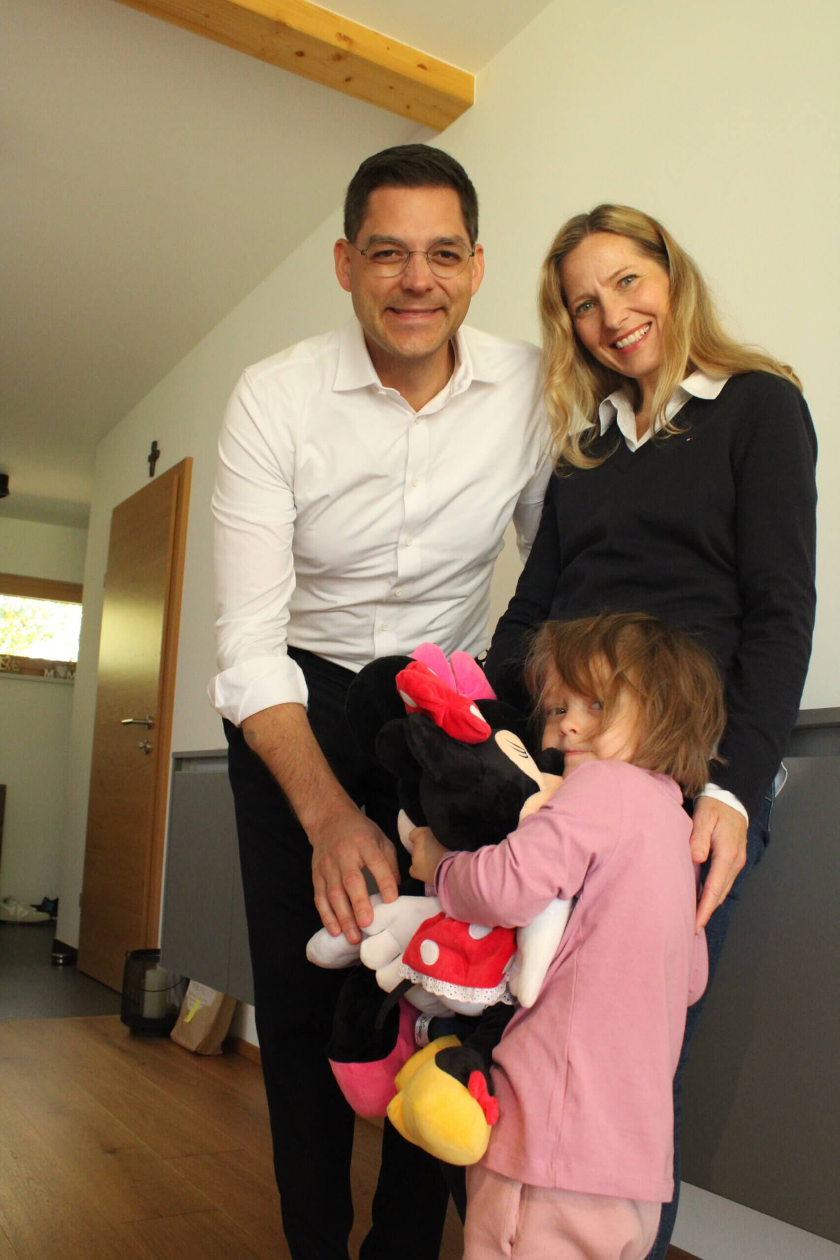 Familienbild: Erwachsene mit Kind und Minnie-Maus-Plüschfigur in einem gemütlichen Raum, lächelnd und harmonisch.