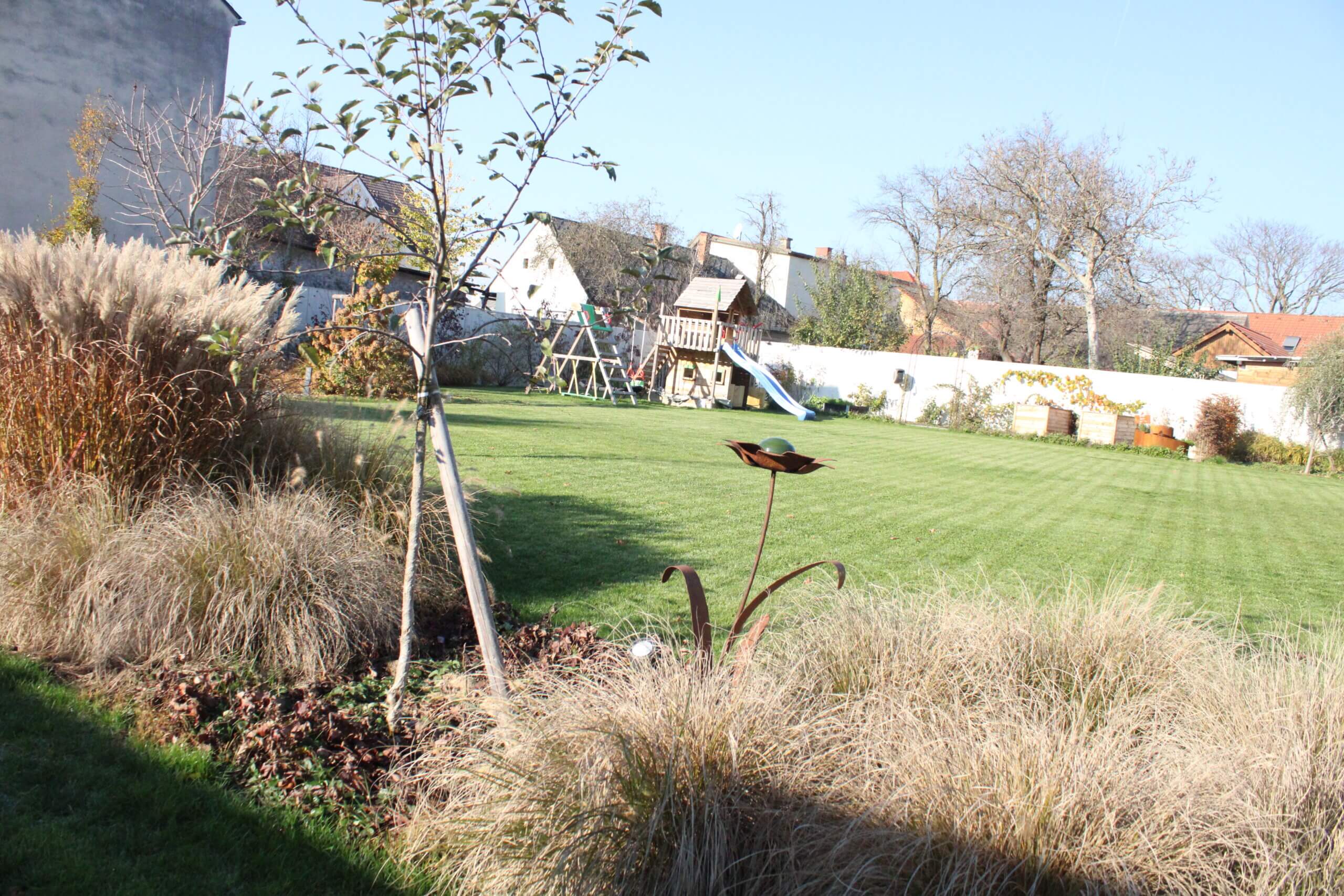 Großer Garten mit Klettergerüst und Rutsche, umgeben von Bäumen und Sträuchern, perfekte Spielfläche für Kinder.