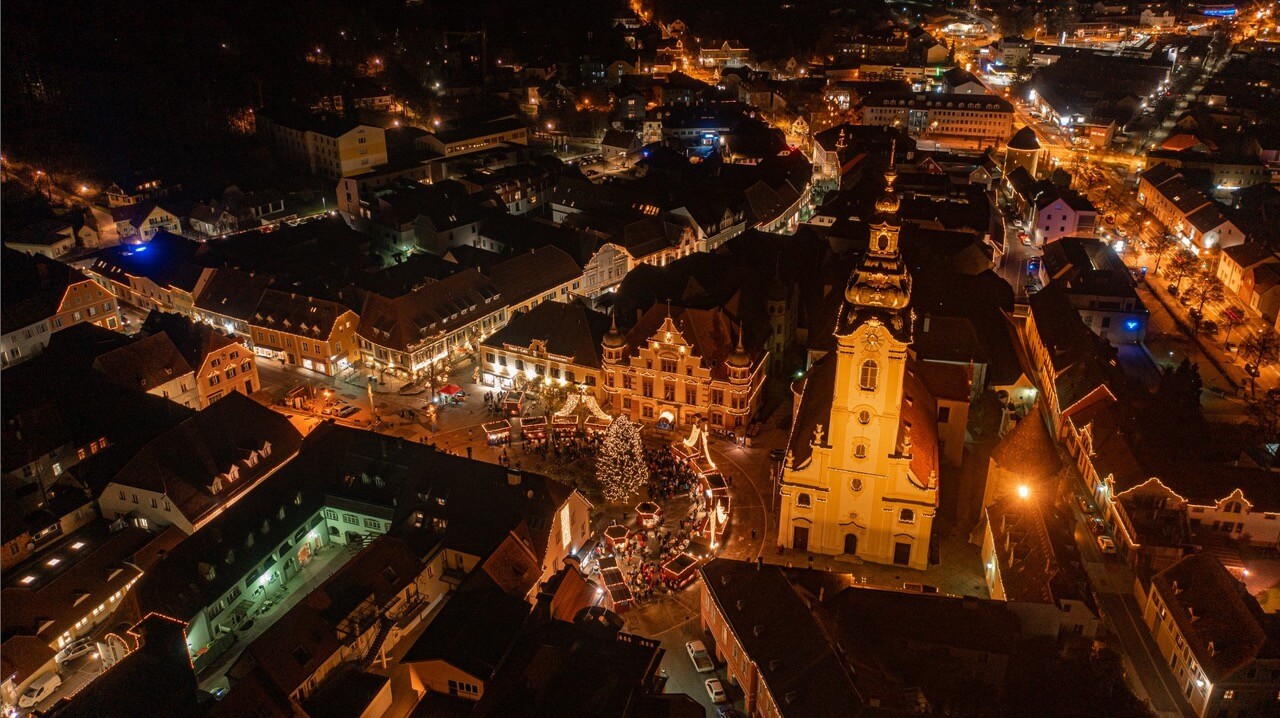 Festlich beleuchteter Weihnachtsmarkt bei Nacht in einer historischen Altstadt mit Kirche und geschmücktem Weihnachtsbaum.
