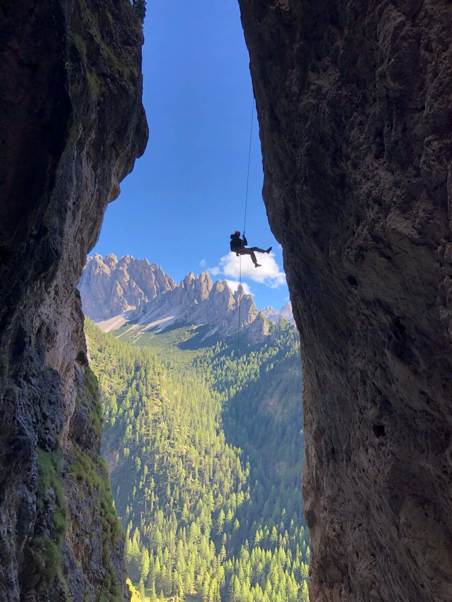 Kletterer seilt sich in spektakulärer Berglandschaft ab, mit Blick auf bewaldete Gipfel und blauem Himmel. Abenteuer in den Alpen.