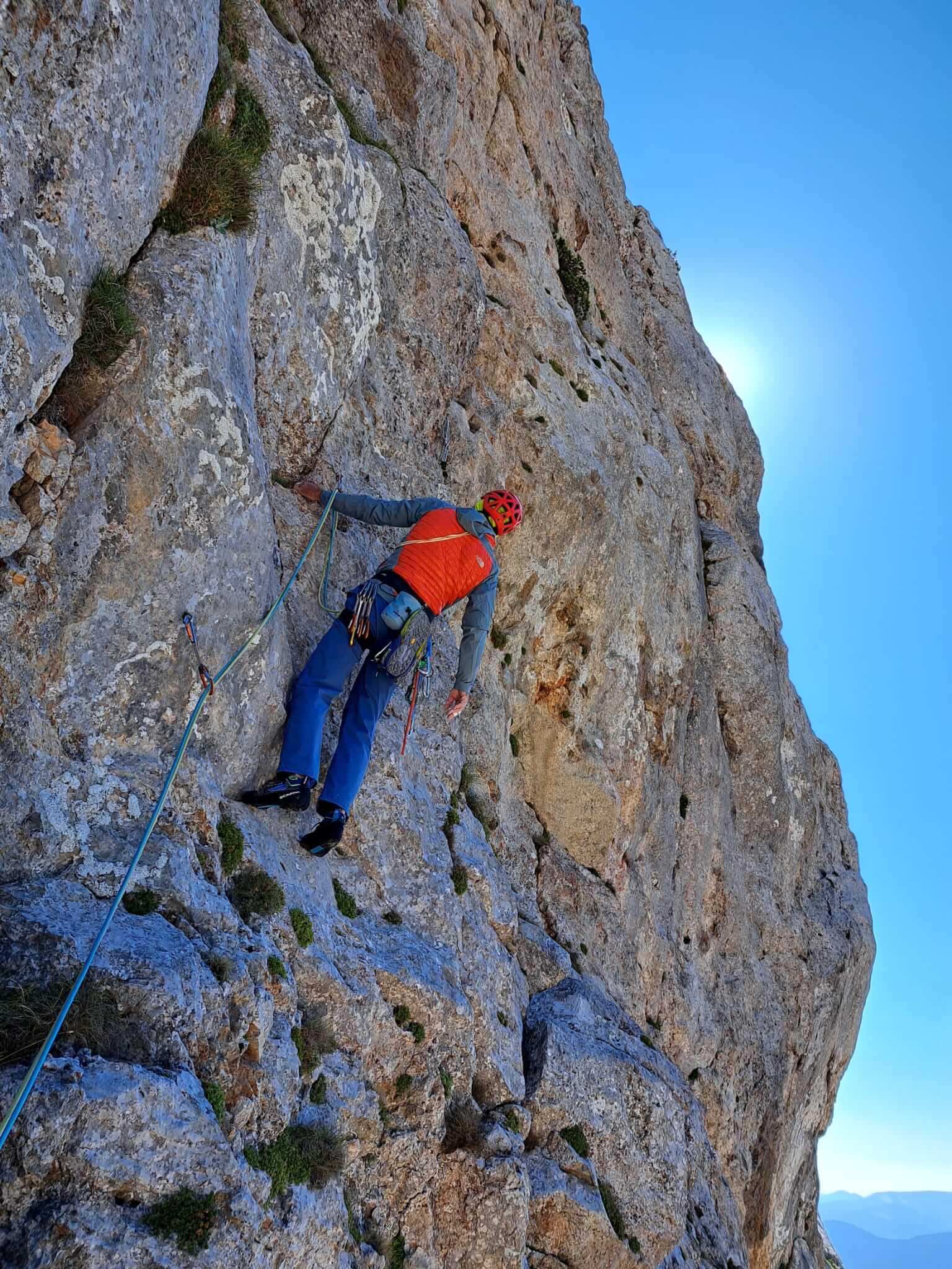 Kletterer in leuchtender Ausrüstung erklimmt eine steile Felswand unter blauem Himmel bei strahlendem Sonnenschein.