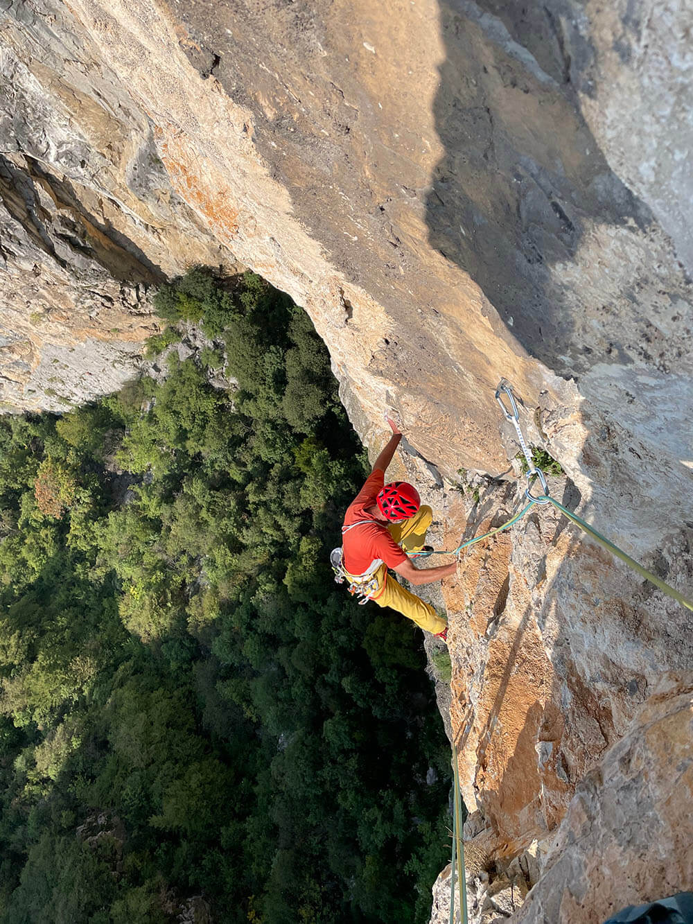 Kletterer in rotem Helm bezwingt steile Felswand mit grüner Waldlandschaft im Hintergrund. Abenteuer und Natur pur.