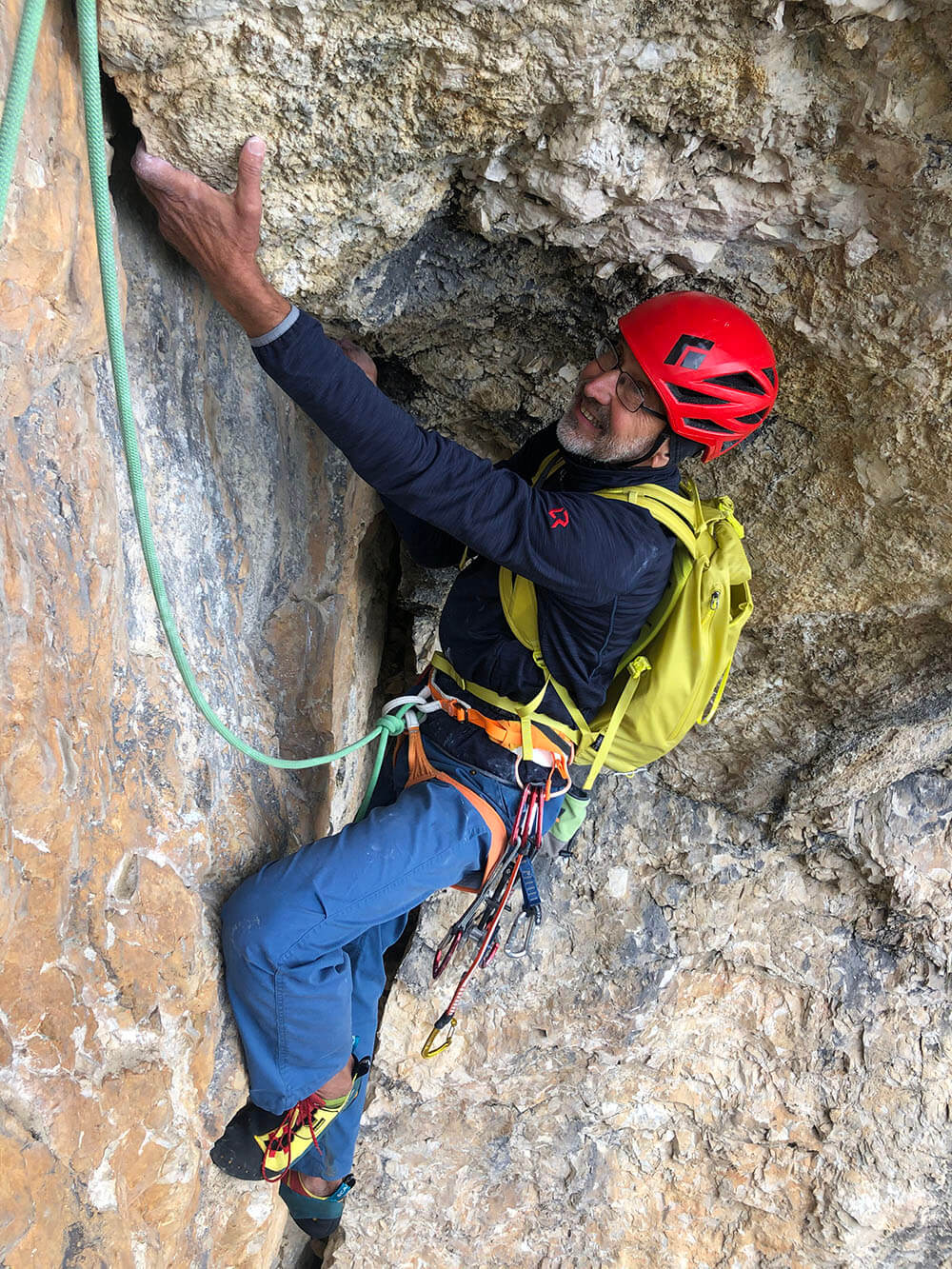 Mann im roten Helm beim Klettern an einer Felswand, Ausrüstung sichtbar, Fokus auf Abenteuer und Outdoor-Aktivität.