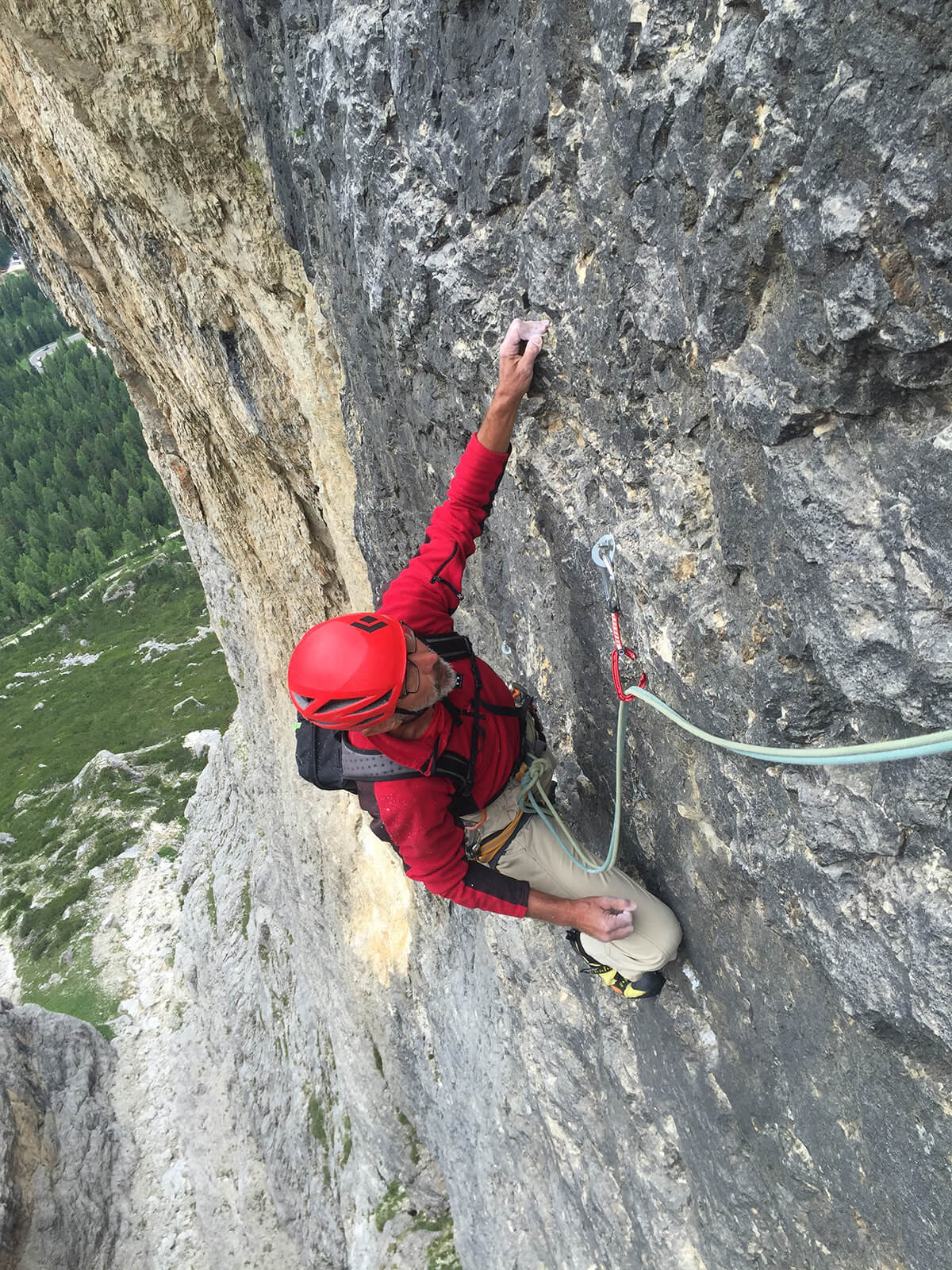 Kletterer in roter Ausrüstung beim Felsenklettern in beeindruckender Höhe, gesichert mit Seil und Karabiner.