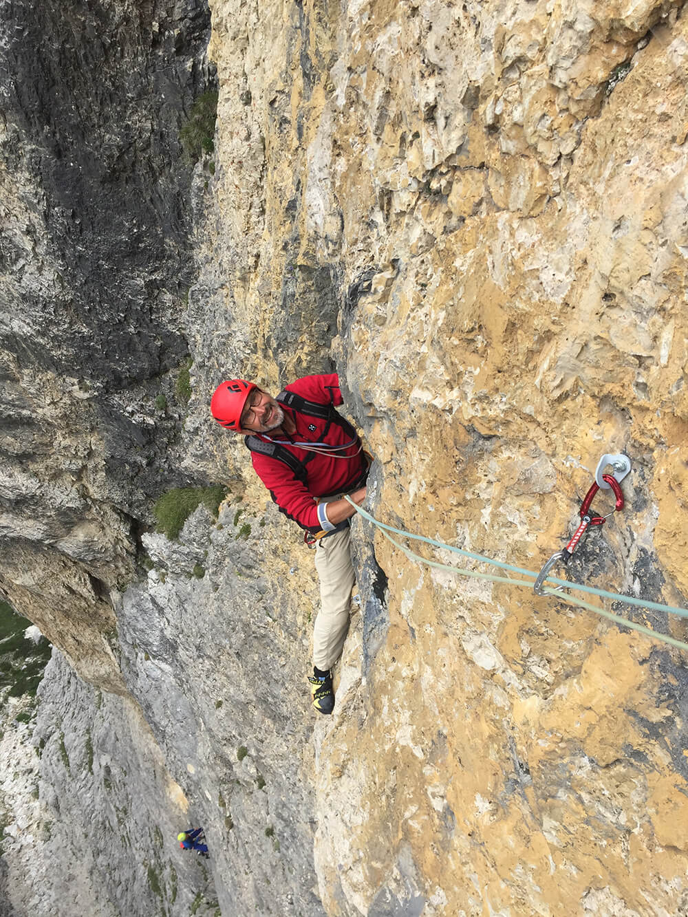 Kletterer in roter Jacke am steilen Felsen, gesichert mit Kletterseil und Karabiner, zeigt Abenteuerlust in felsiger Landschaft.