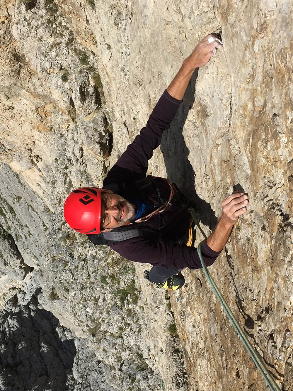 Kletterer mit rotem Helm erklimmt steile Felswand, konzentriert und gesichert, unter klarem Himmel. Abenteuer und Natur erleben.