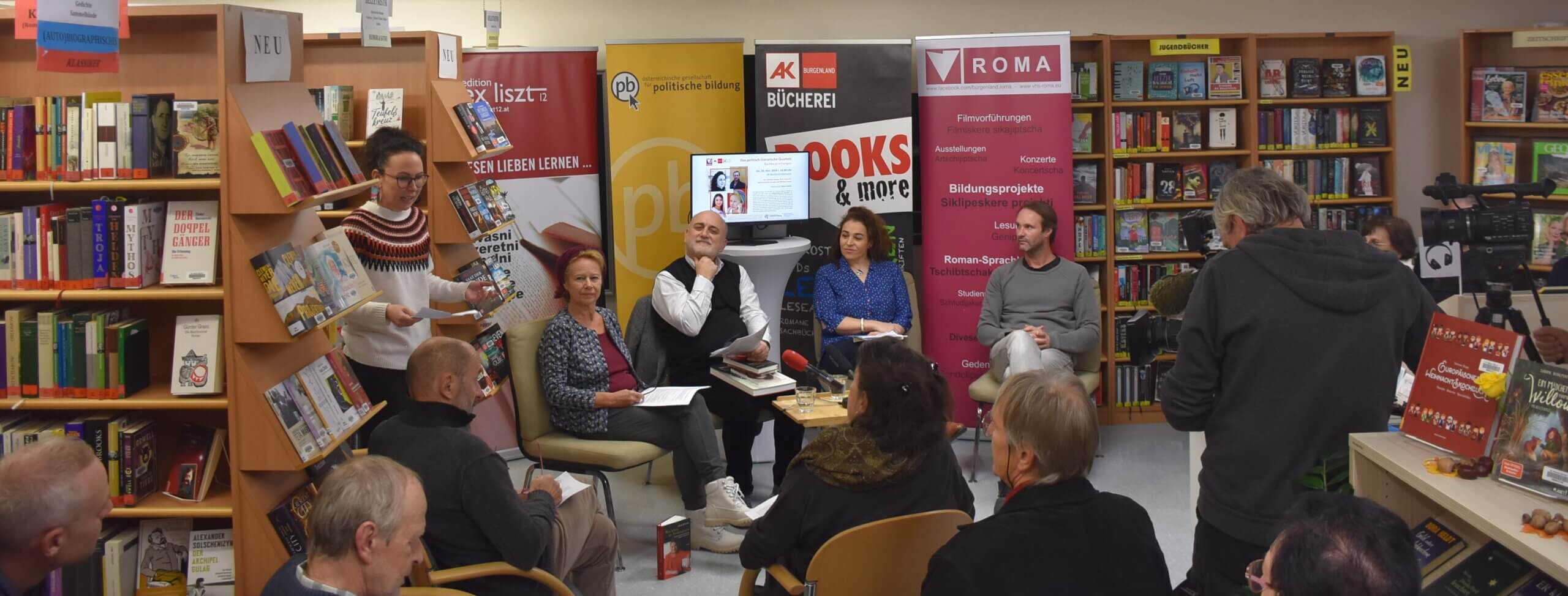 Lesung in einer Buchhandlung mit mehreren Personen, die aufmerksam einem Referenten zuhören.