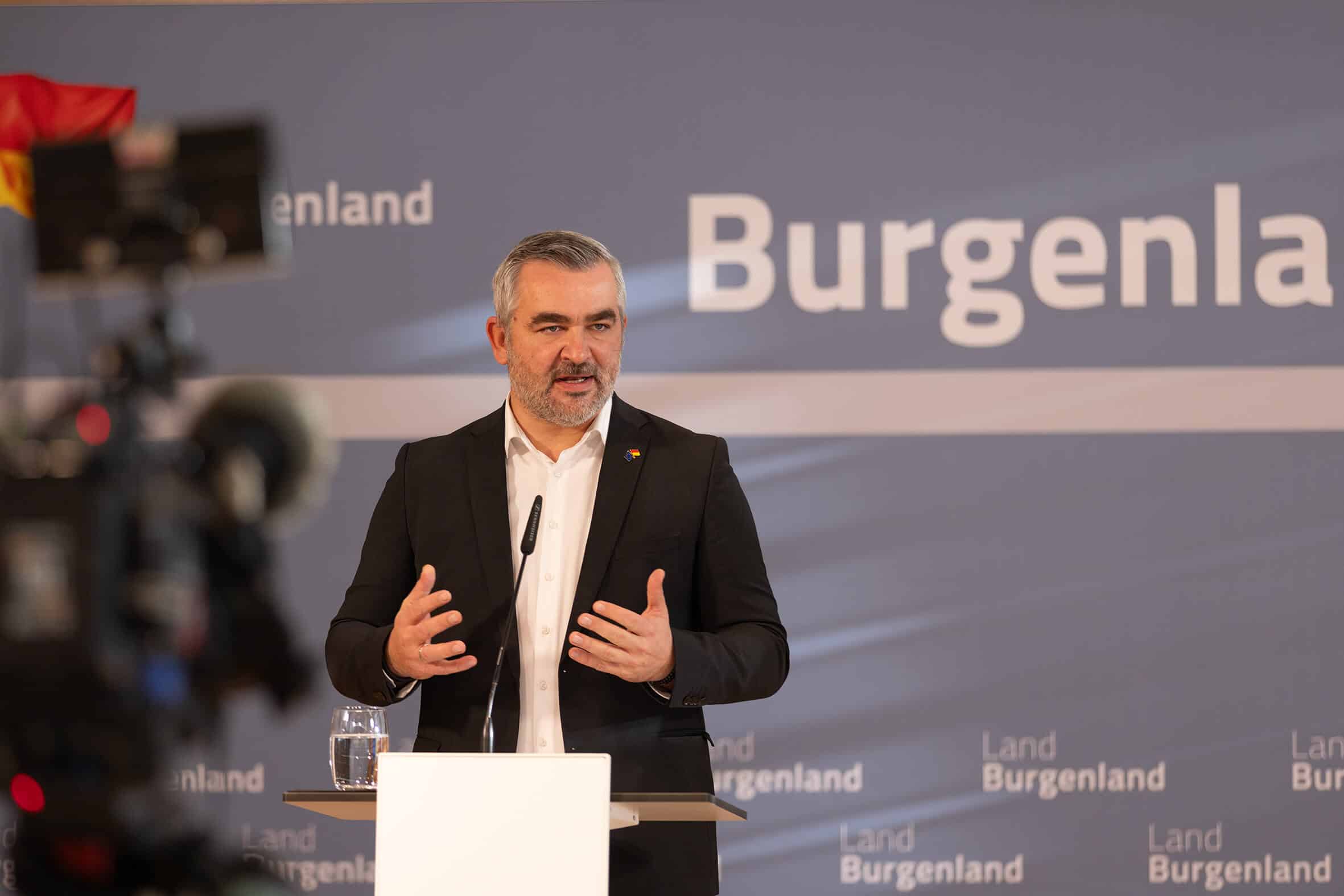 Landesrat Heinrich Dorner hält Rede bei Pressekonferenz in Burgenland, vor Kamera und Mikrofon, trägt Anzug und spricht engagiert.