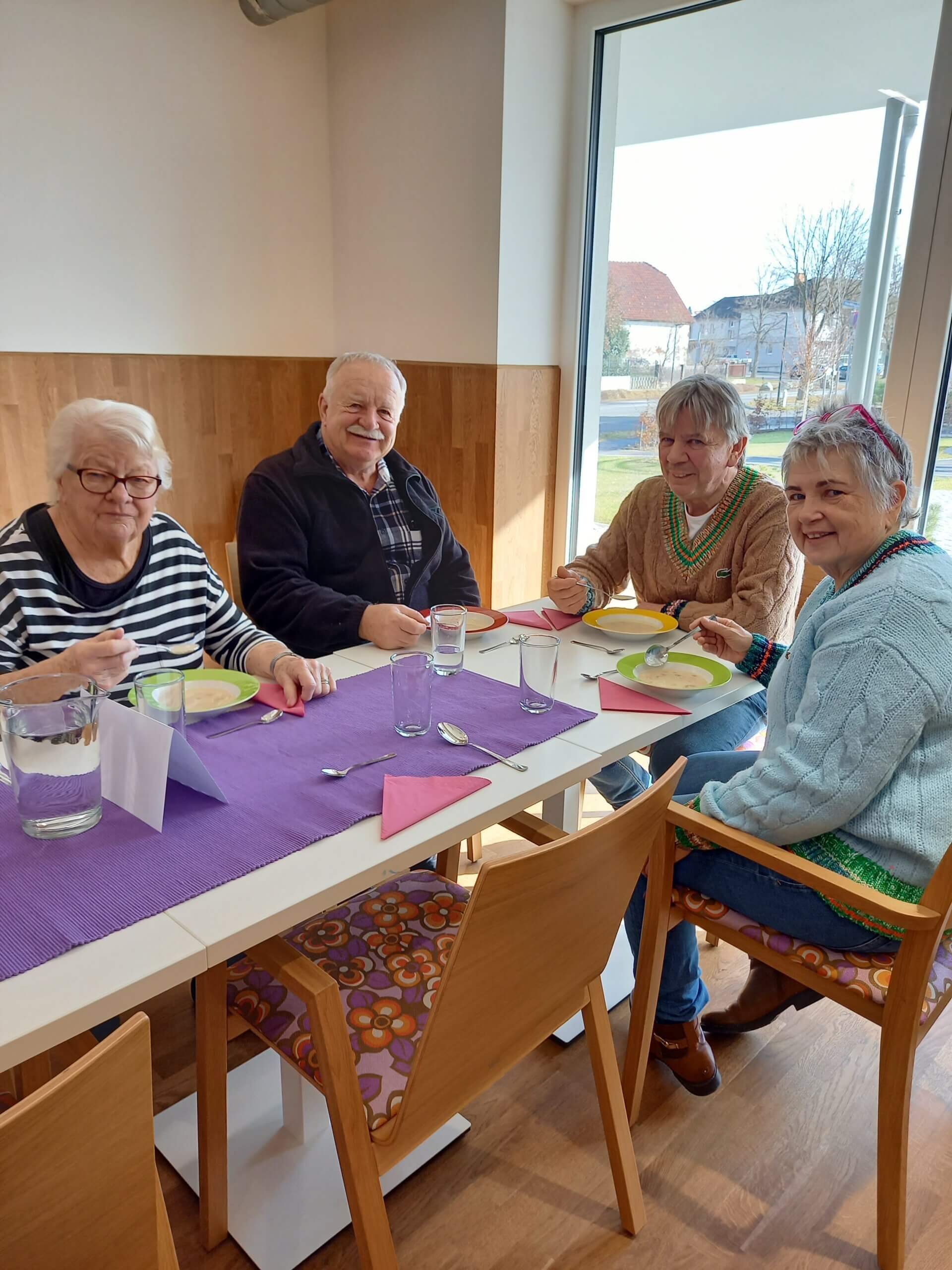 Senioren genießen gemeinsam eine Mahlzeit an einem hellen Frühstückstisch im Pflegeheim.