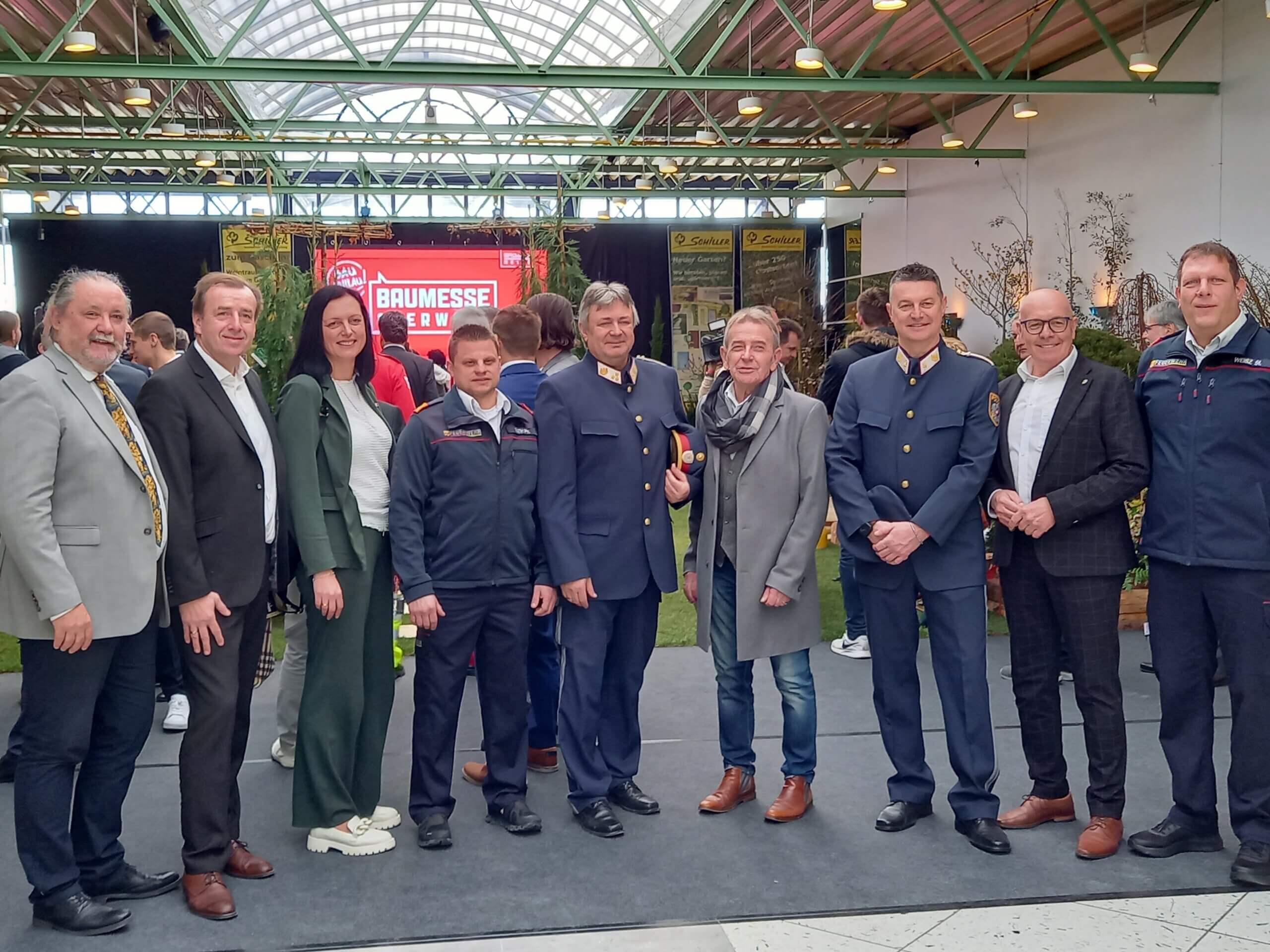 Gruppe von Menschen bei der Baumesse 2023, einige in Uniformen, vor einem Messestand in einer Halle.