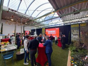 Besucher bei der Baumesse Oberwart 2023, diskutieren und informieren sich an verschiedenen Ständen in einer Messehalle.