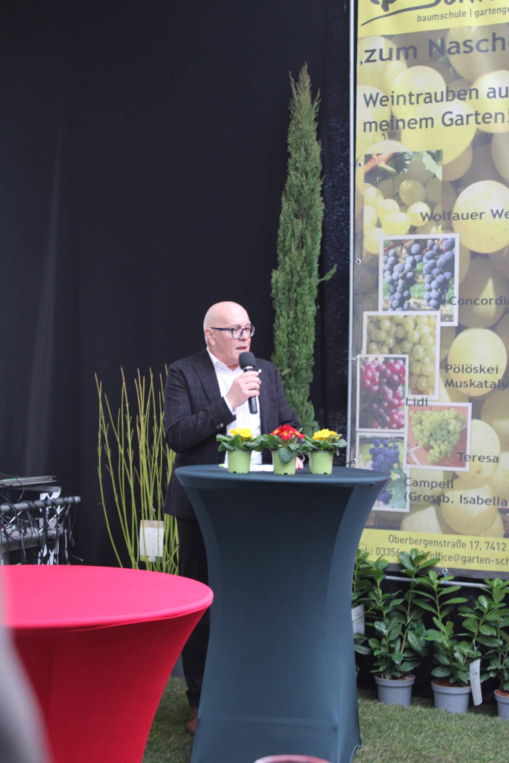 Ein Mann hält eine Rede bei einer Veranstaltung zum Thema Gartenbau und Weintraubenpflege.