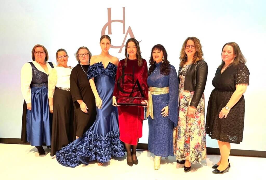 haute-couture-austria-award-2024--burgenlaenderinnen©mohapp Gruppe von Frauen in festlicher Kleidung bei einer Preisverleihung und eine Frau hält eine Auszeichnungstrophäe.