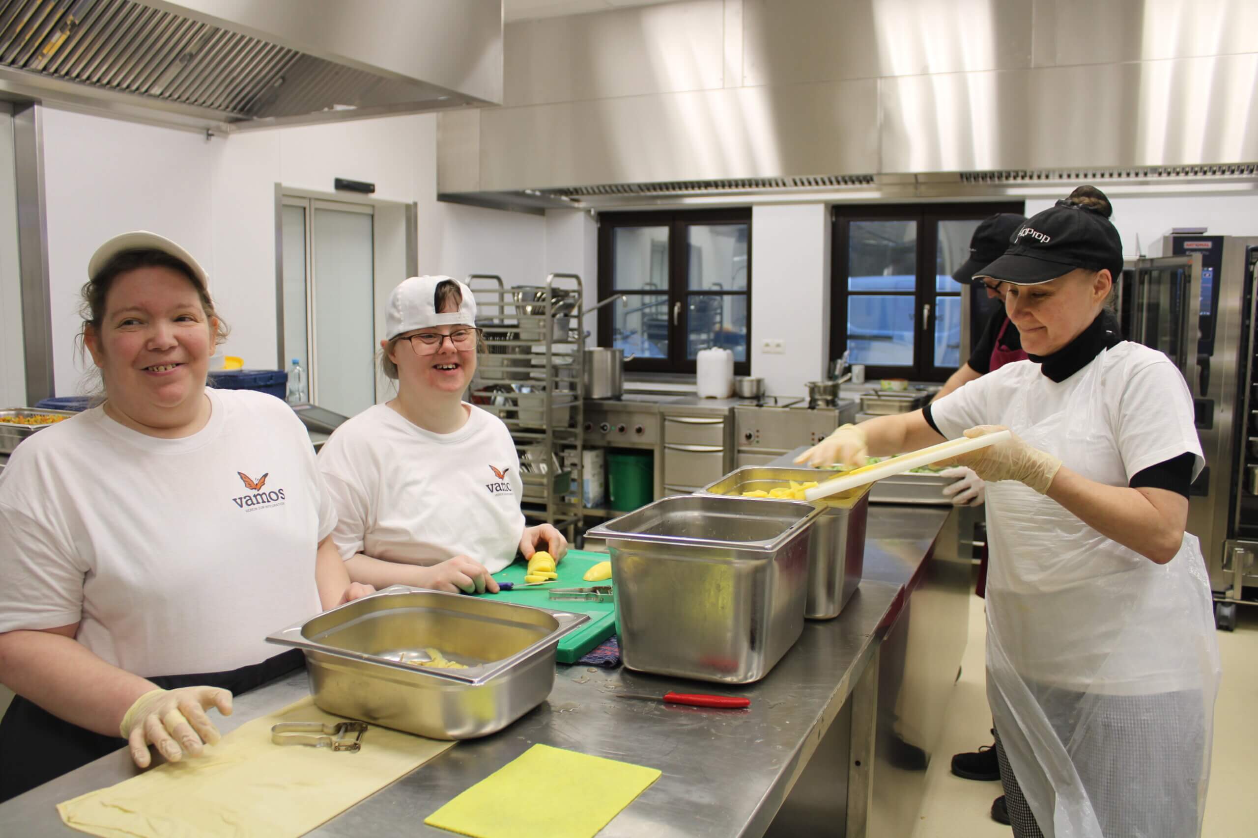Menschen arbeiten gemeinsam in einer Großküche und schneiden Zutaten für das gemeinsame Kochen und Zubereiten von Speisen.