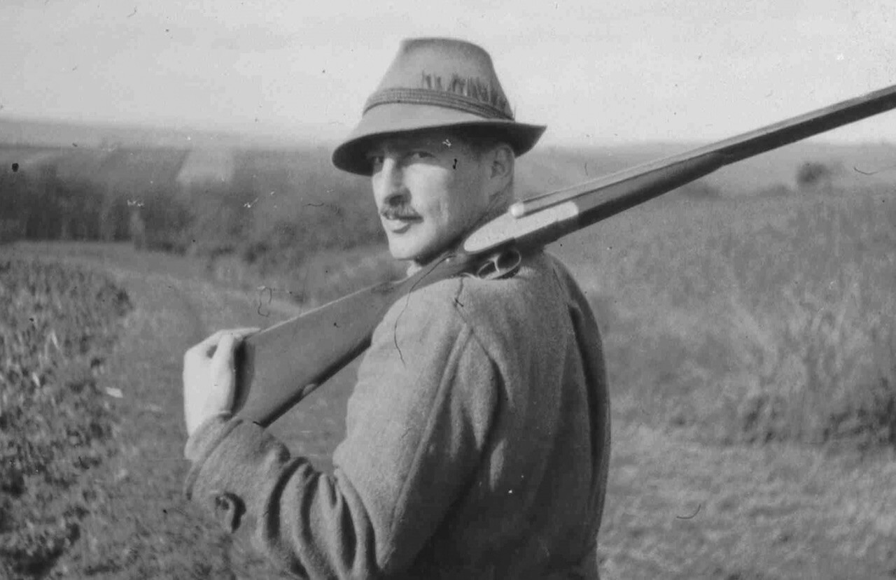 Mann mit Hut und Gewehr auf der Schulter in ländlicher Umgebung. Vintage-Fotografie eines Jägers in der Natur.