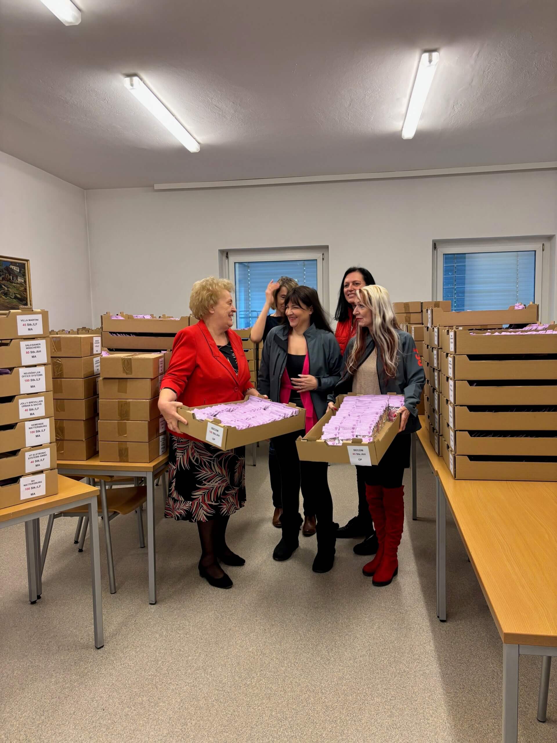 Frauen stehen in einem Raum mit Kartons und sortieren Tücher, Teamarbeit in einer Organisation.