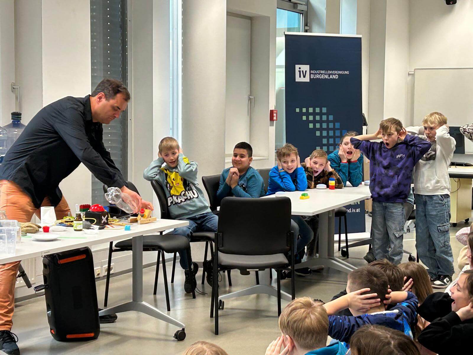 Mann führt Wissenschaftsexperiment vor, umgeben von erstaunten und neugierigen Kindern in einem Klassenzimmer.