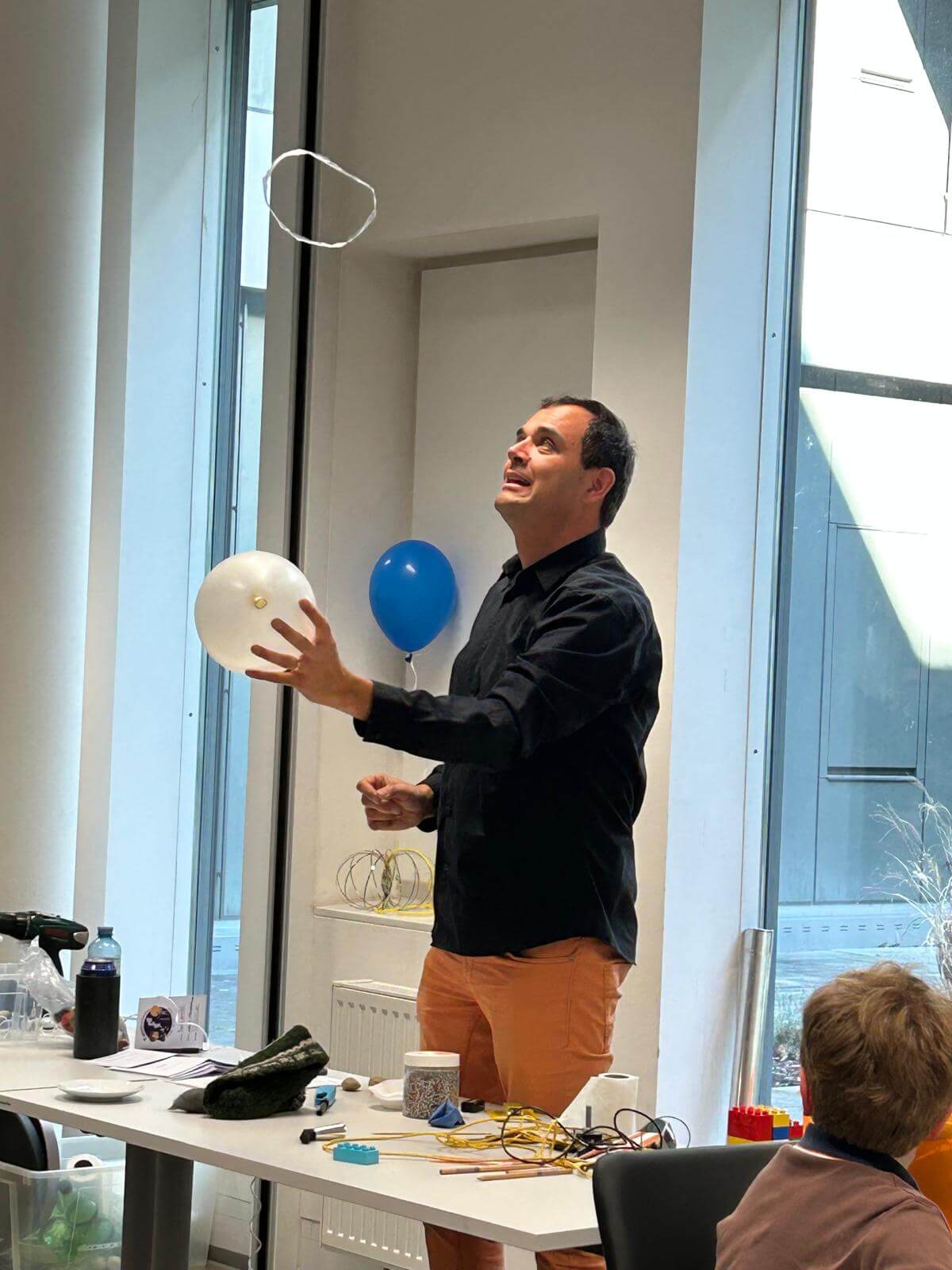 Mann zeigt Experiment mit Ballon und Rauchring in modernem Klassenzimmer vor jungem Publikum.