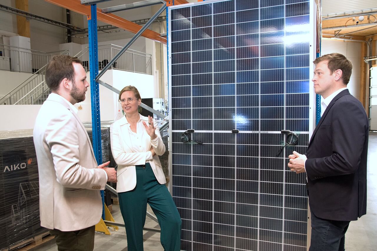 Personen diskutieren neben Solarpanelen in einer Lagerhalle. Solarenergie, erneuerbare Energien, Technologie.