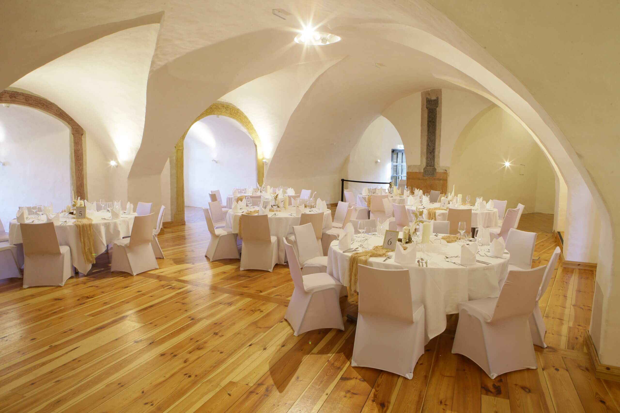 Eleganter Veranstaltungssaal mit gewölbter Decke und stilvoll gedeckten Tischen für ein festliches Dinner.