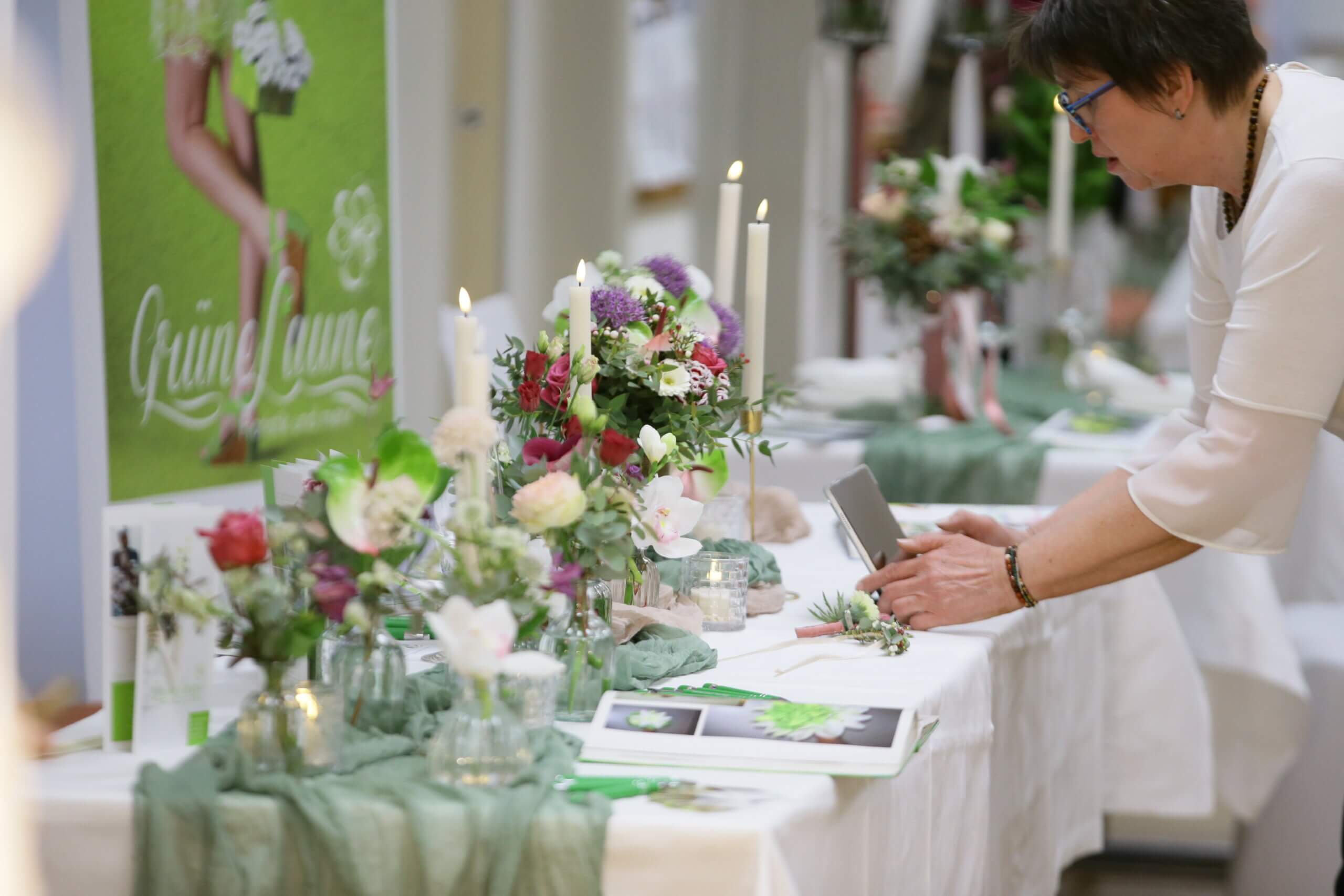 Frau arrangiert Blumen auf Hochzeitstisch mit Kerzen und Dekoration für Eventausstellung.