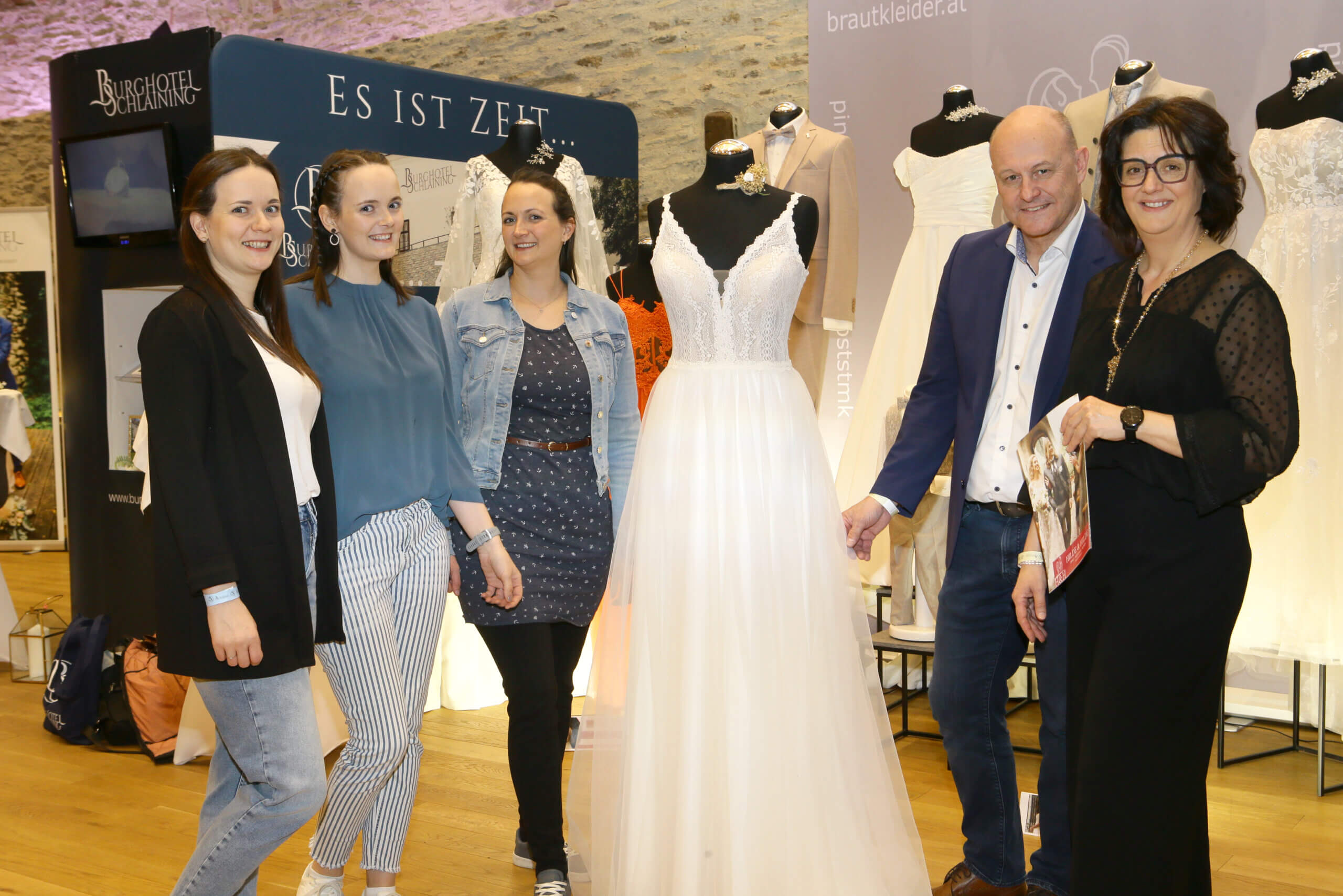 Menschen neben Hochzeitskleidern bei einer Brautmodenausstellung im Burghotel Schlaining.