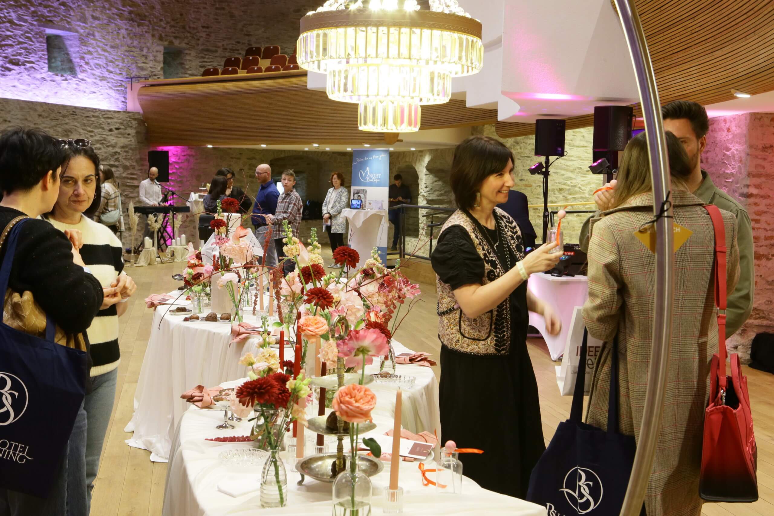 Gesprächsrunde auf einer Hochzeitmesse, elegantes Ambiente mit Blumenarrangements und Kristallleuchtern.