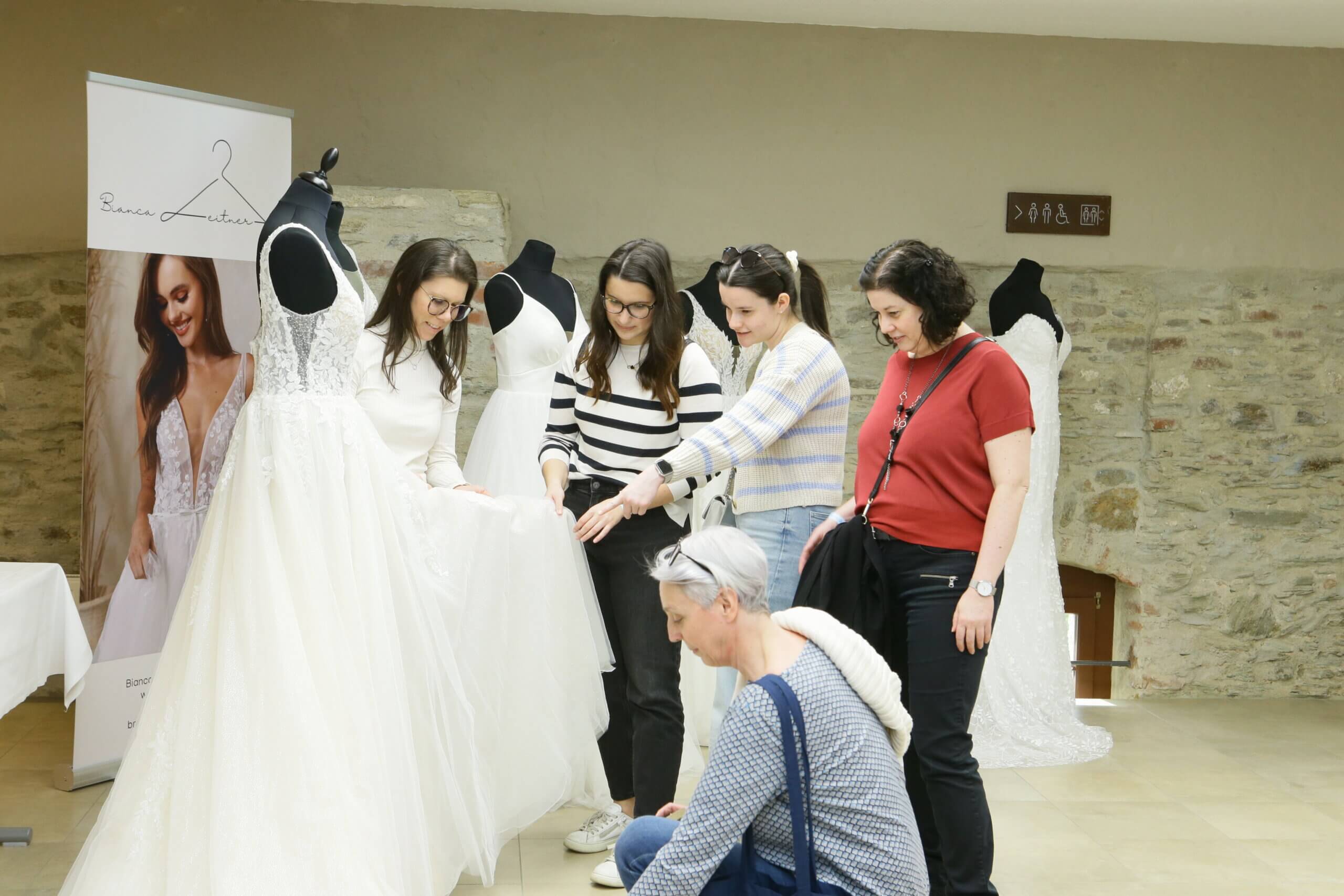 Gruppe von Frauen betrachtet zusammen ein elegantes Hochzeitskleid auf einer Modenschau.