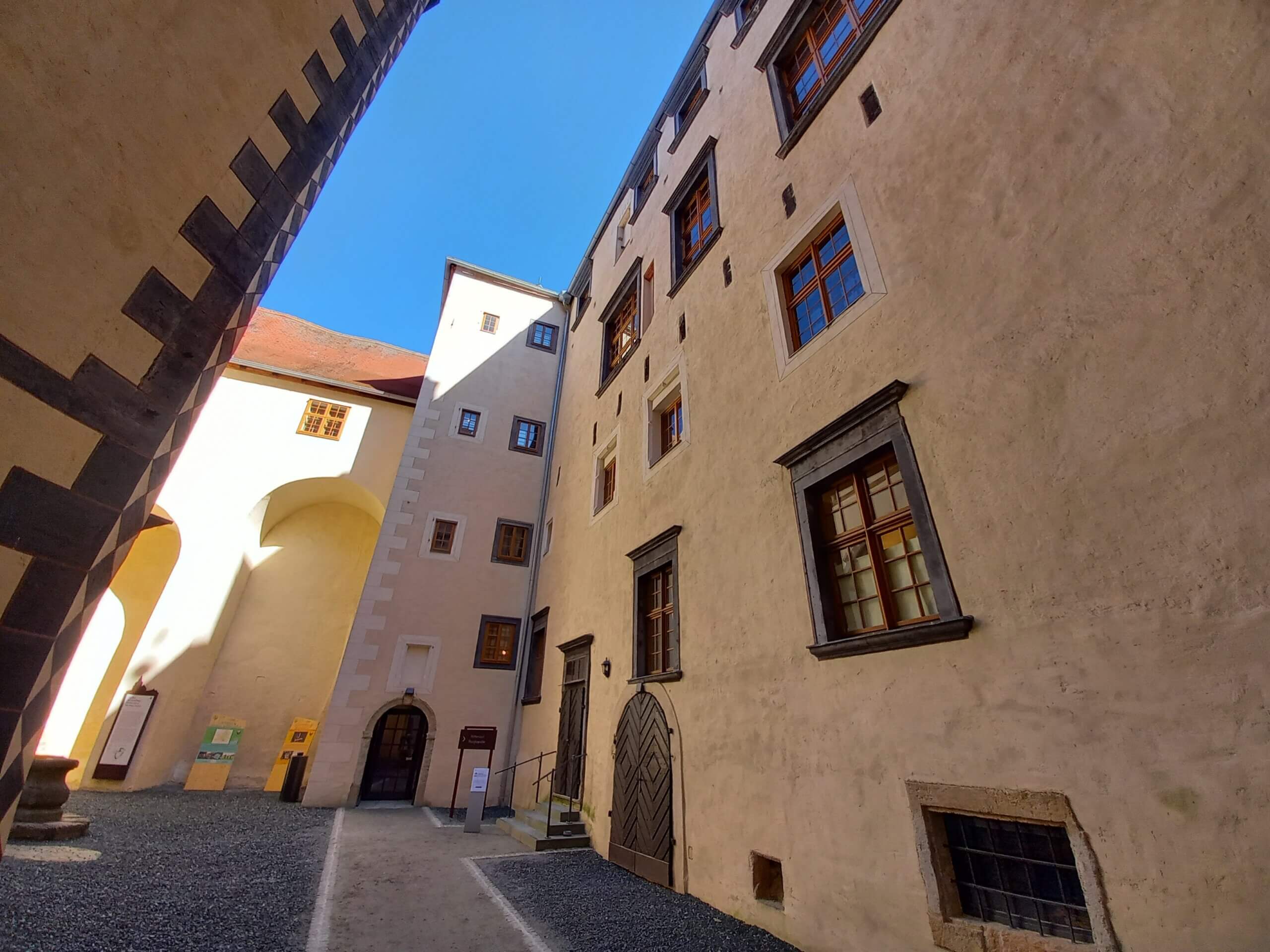 Innenhof eines historischen Gebäudes mit gepflastertem Boden und hohen, fensterreichen Mauern unter blauem Himmel.
