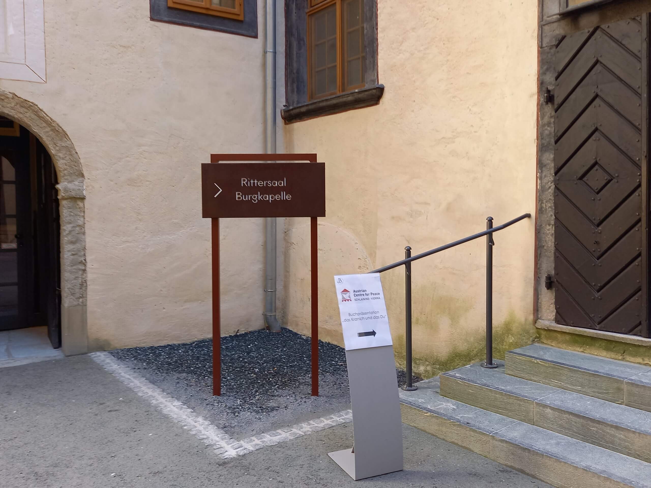 Wegweiser zur Burgkapelle und zum Rittersaal an einer Altstadt-Fassade mit Treppe und Holztür.