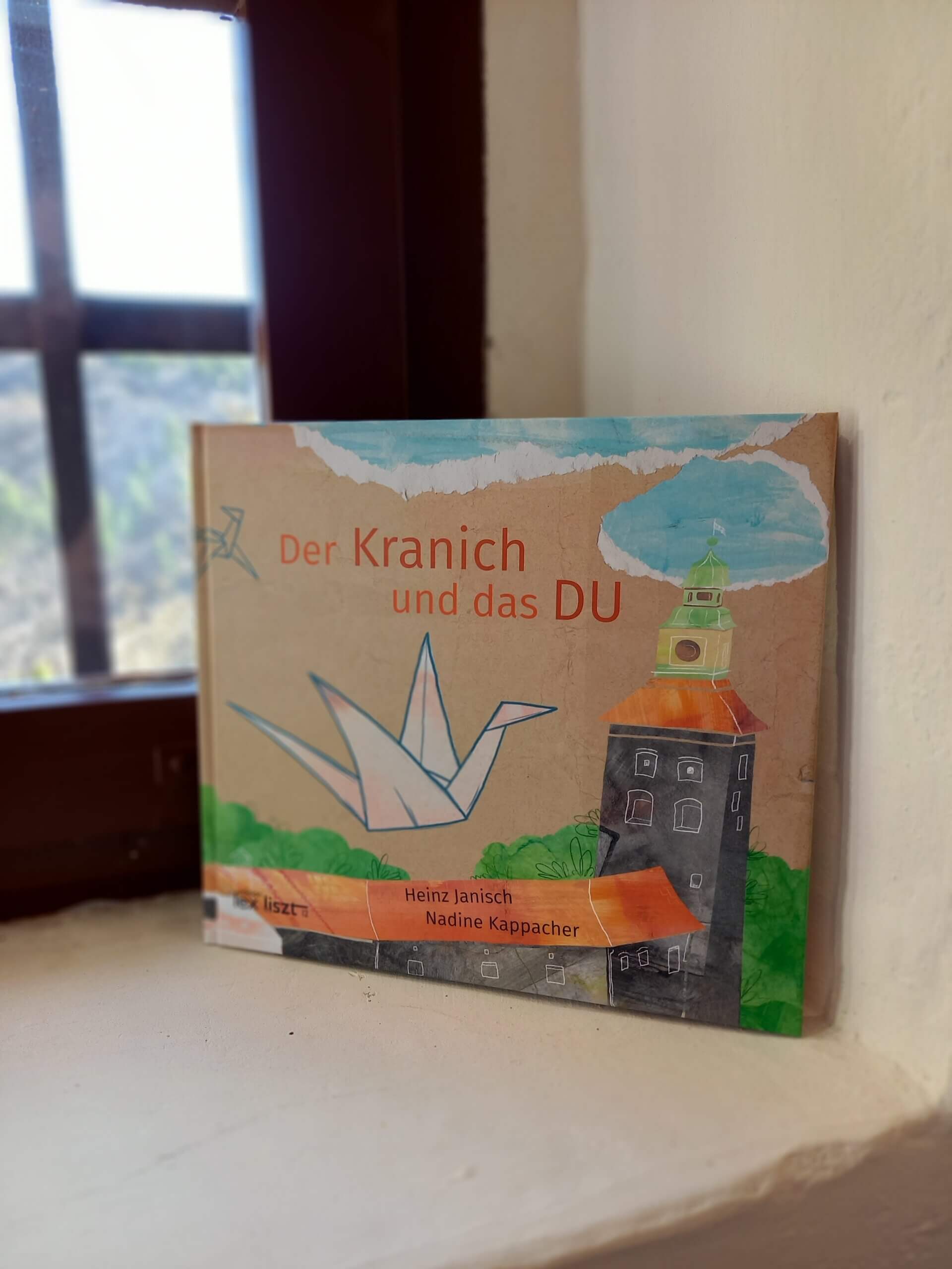 Kinderbuch Der Kranich und das DU von Heinz Janisch und Nadine Kappacher, gelehnt am Fensterbrett.