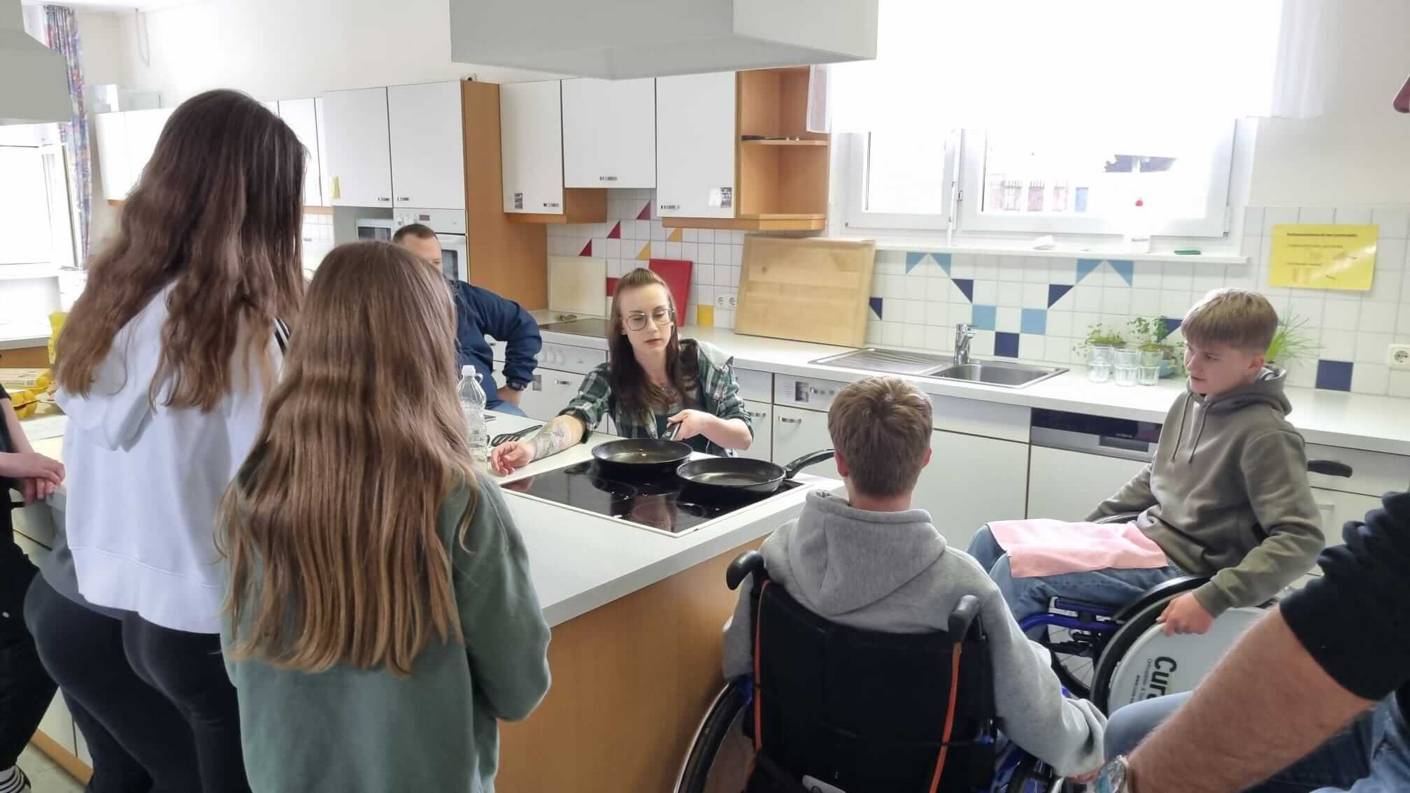 Gruppe von Personen kocht in heller Küche, inklusive Person im Rollstuhl beim Kochkurs.