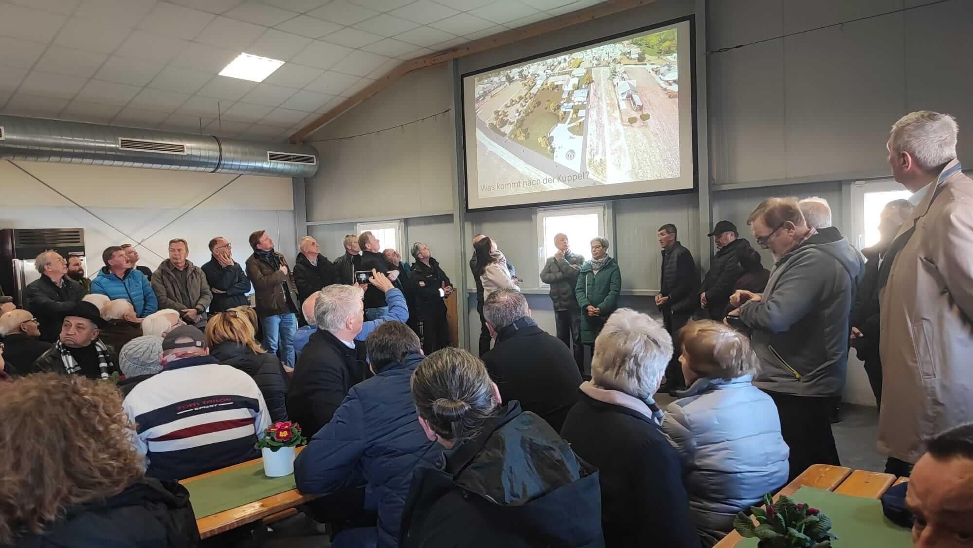 Versammlung in einem Besprechungsraum mit Personen, die eine Präsentation über zukünftige Pläne auf einer Leinwand ansehen.