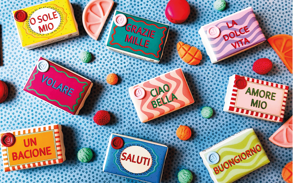 Bunte Seifenstücke mit italienischen Aufschriften auf einem gepunkteten Hintergrund, dekoriert mit Obstformen.