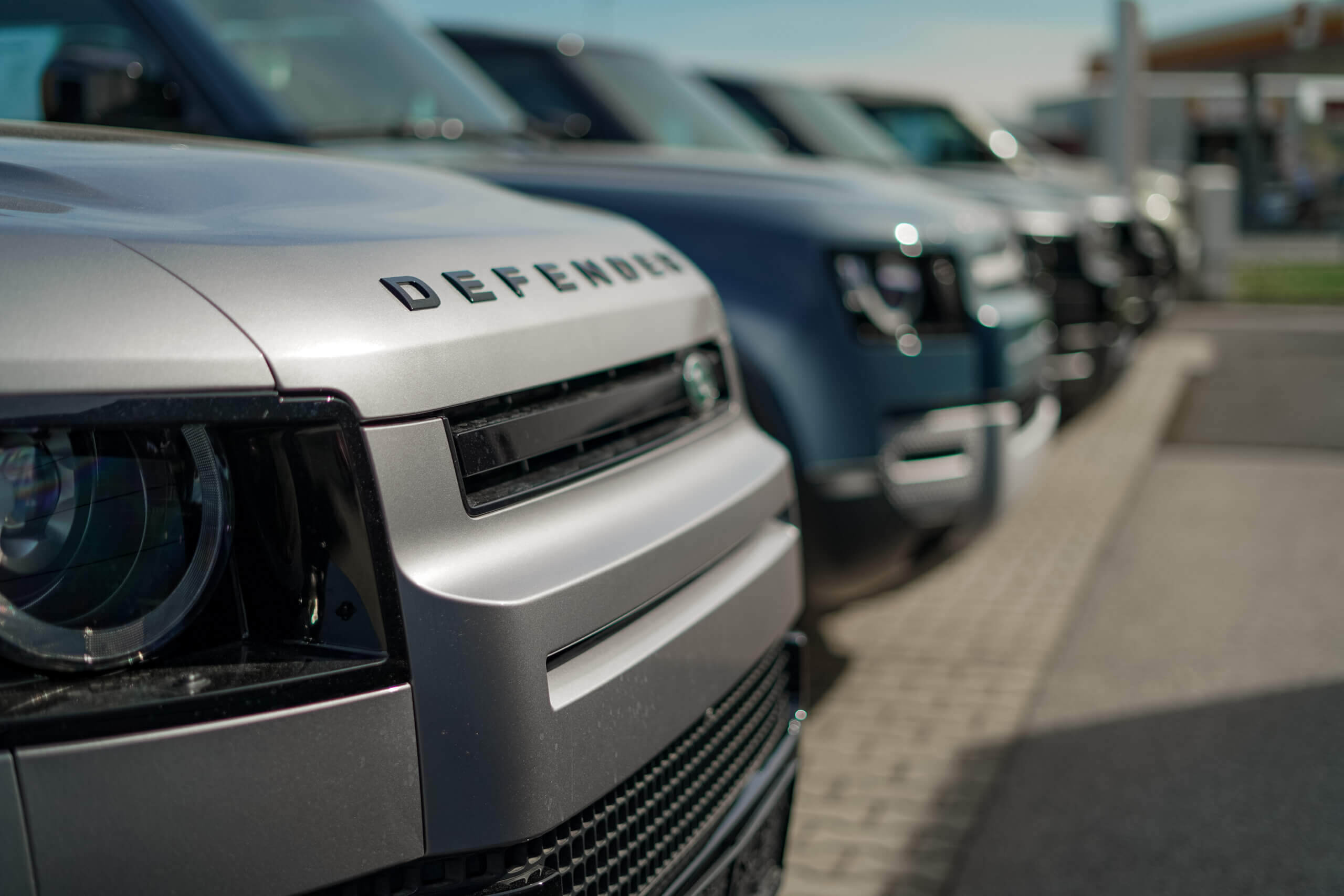 Reihe von neuen Defender-Geländewagen in einem Autohaus, seitliche Nahaufnahme, um Umweltfreundlichkeit zu betonen.