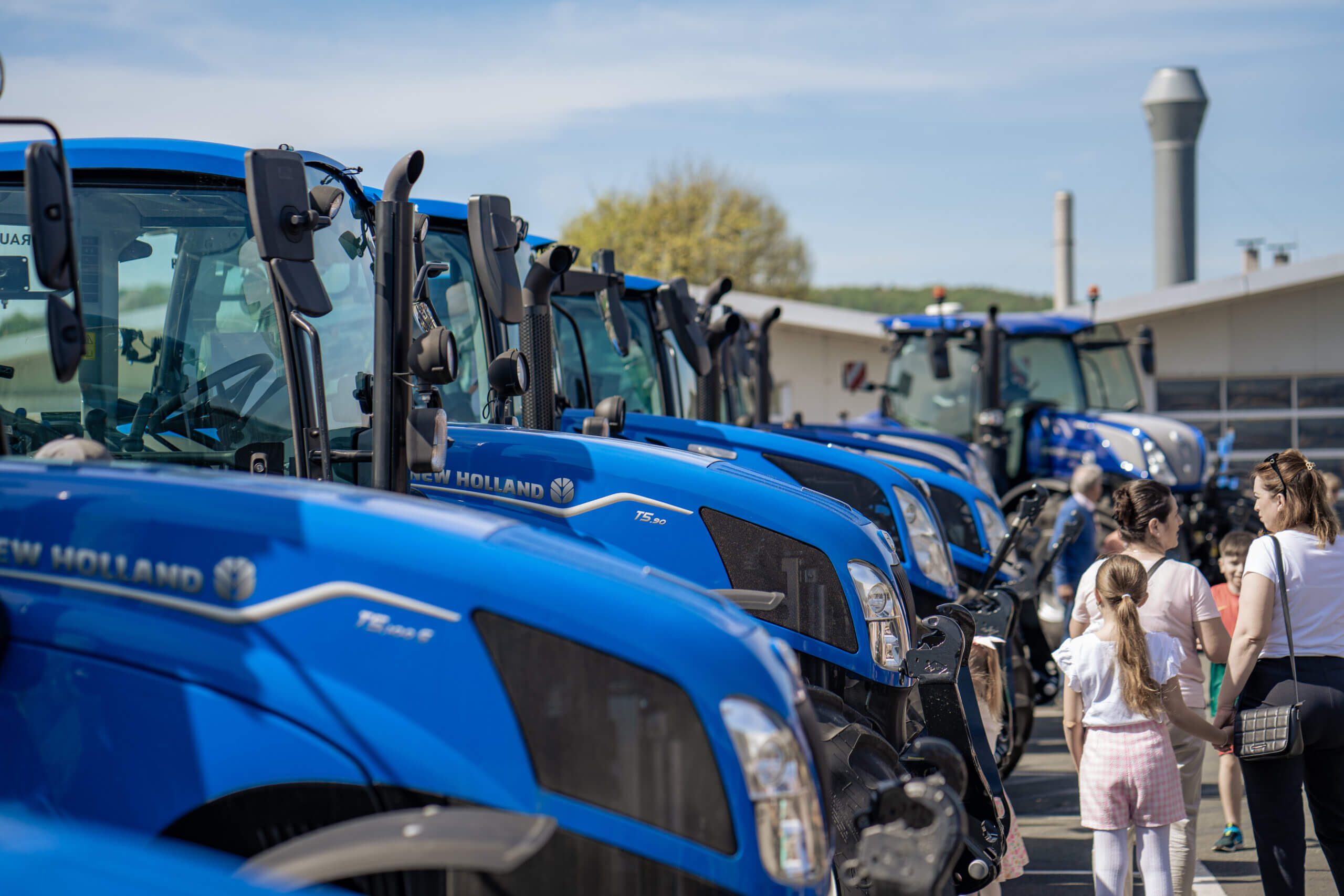 Reihe blauer Traktoren und Menschen bei einer Außenveranstaltung an einem sonnigen Tag.