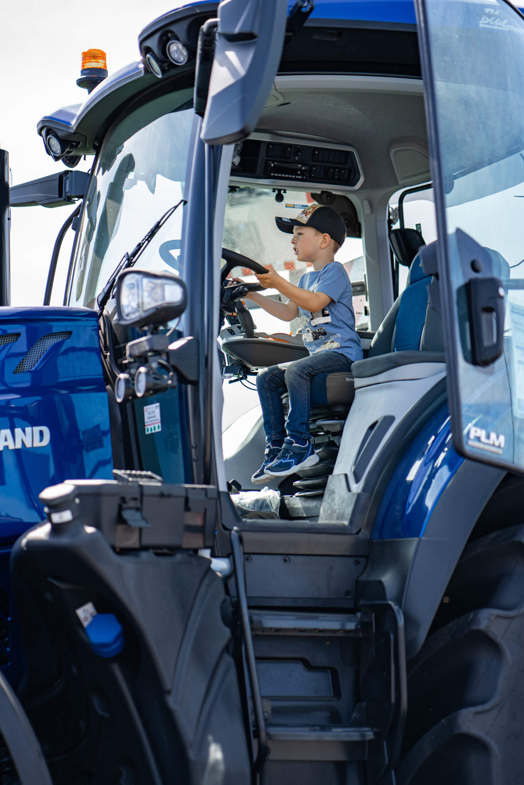 Junge im blauen Traktor sitzend, trägt Mütze, schaut aufmerksam, ländliche Szene, Kinder erleben Landwirtschaft.