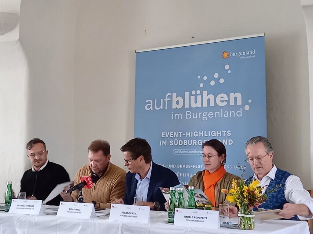 Pressekonferenz Aufblühen im Burgenland mit Personen am Tisch, Veranstaltungsdetails, Blumenarrangement.