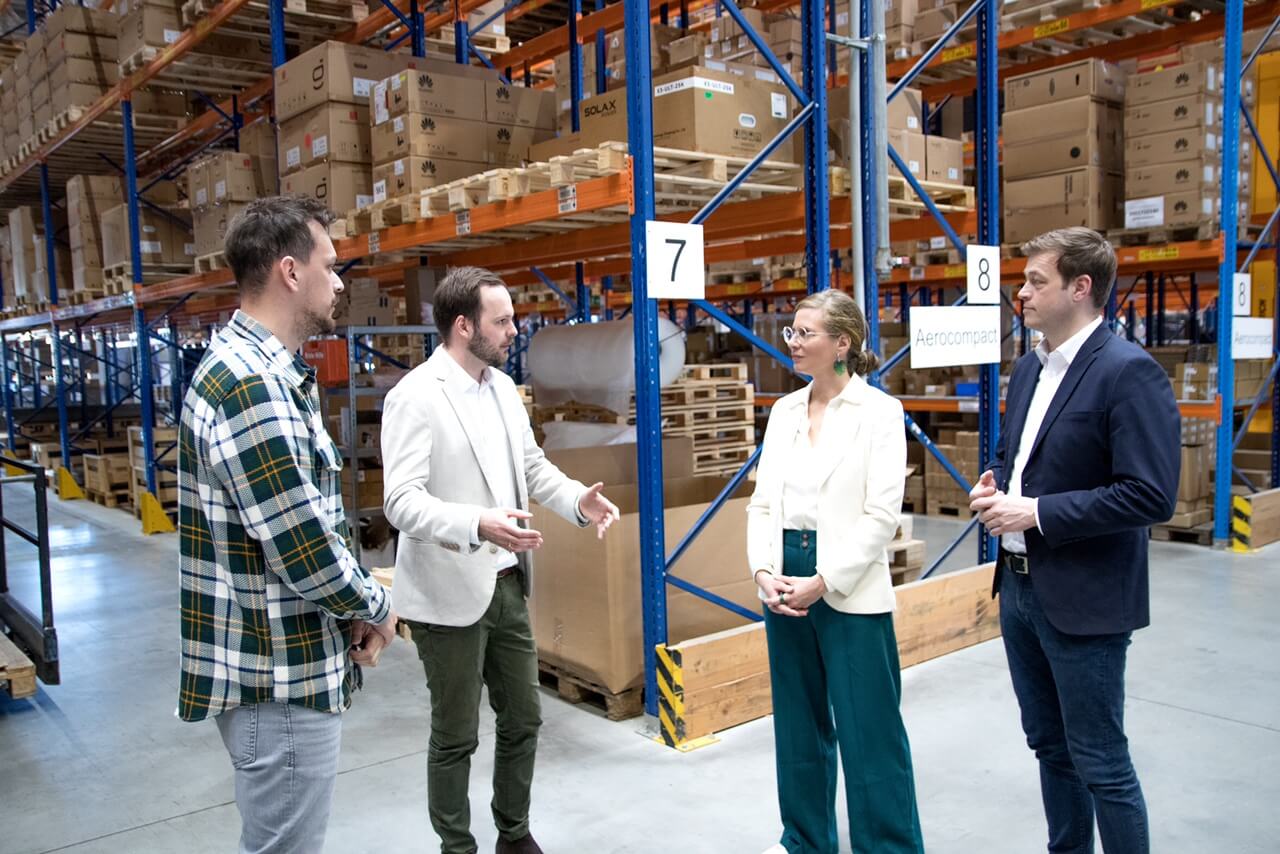 Personen diskutieren in einem großen Lager mit Regalen voller Kartons.