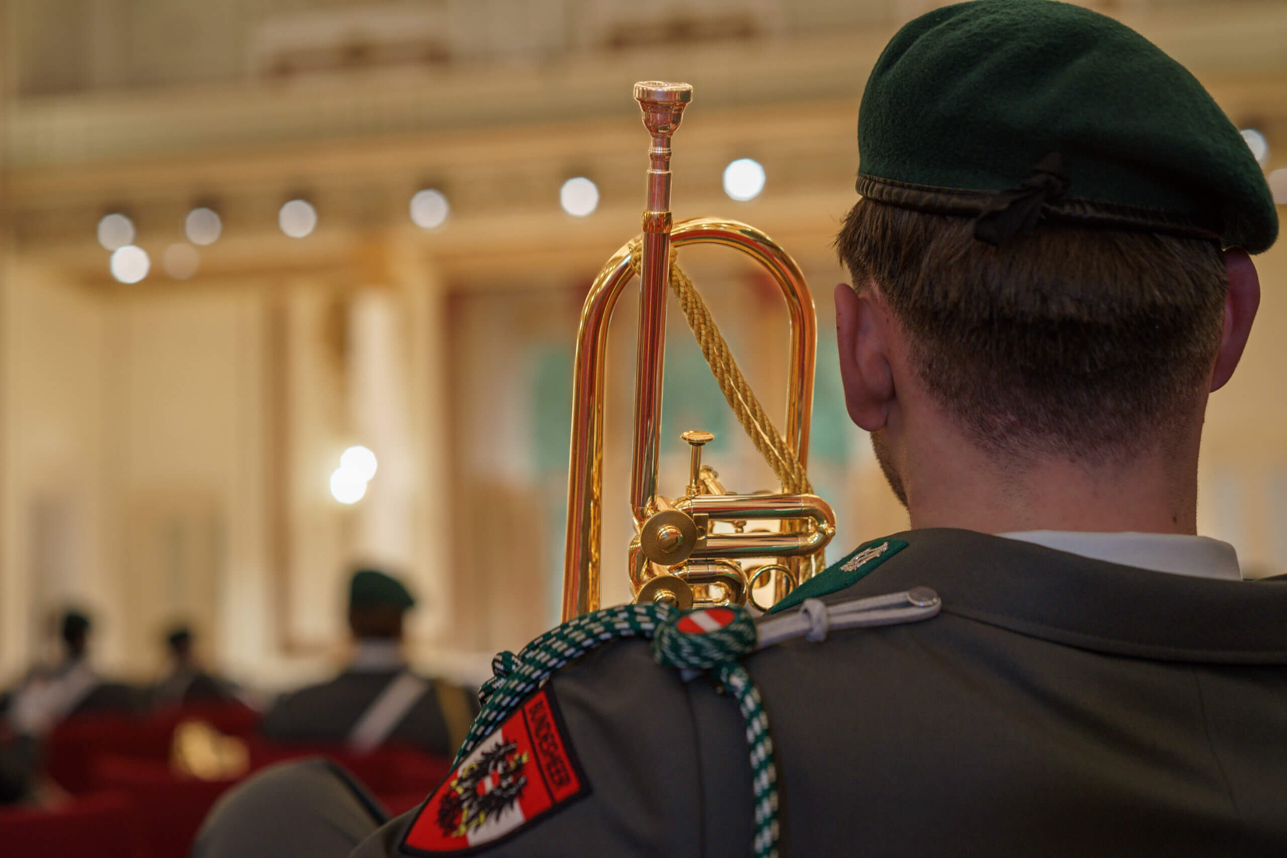 Soldat in Uniform spielt Trompete bei einer Zeremonie in einem eleganten, beleuchteten Saal.
