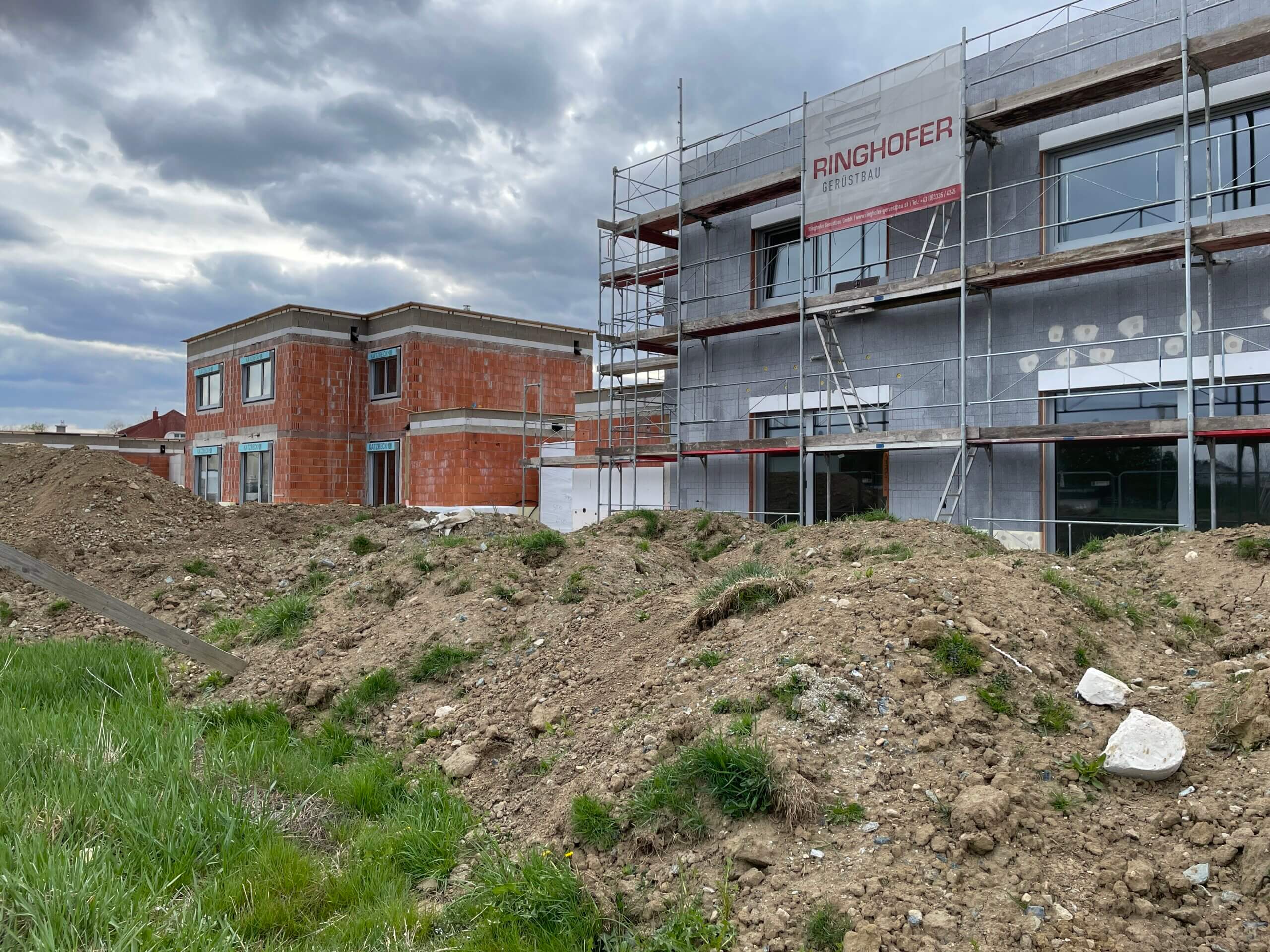 Neubau von Häusern mit Gerüst, stürmische Wolken und Erdaufschüttungen im Vordergrund.